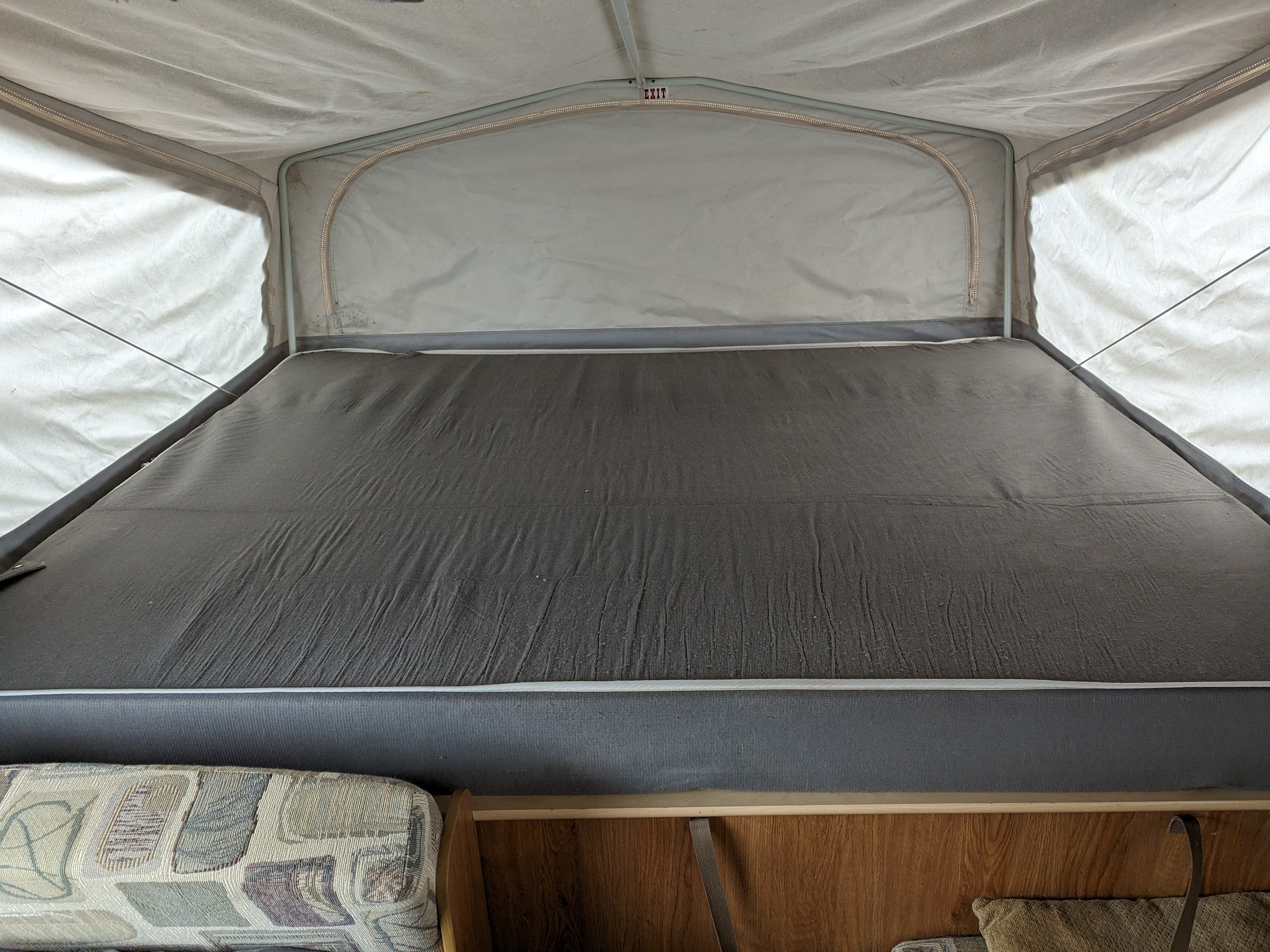 Inside an RV rental pop-up camper, featuring a large gray mattress, light fabric walls with zippers, and an overhead 'EXIT' sign.. Jayco Ultralite 2008