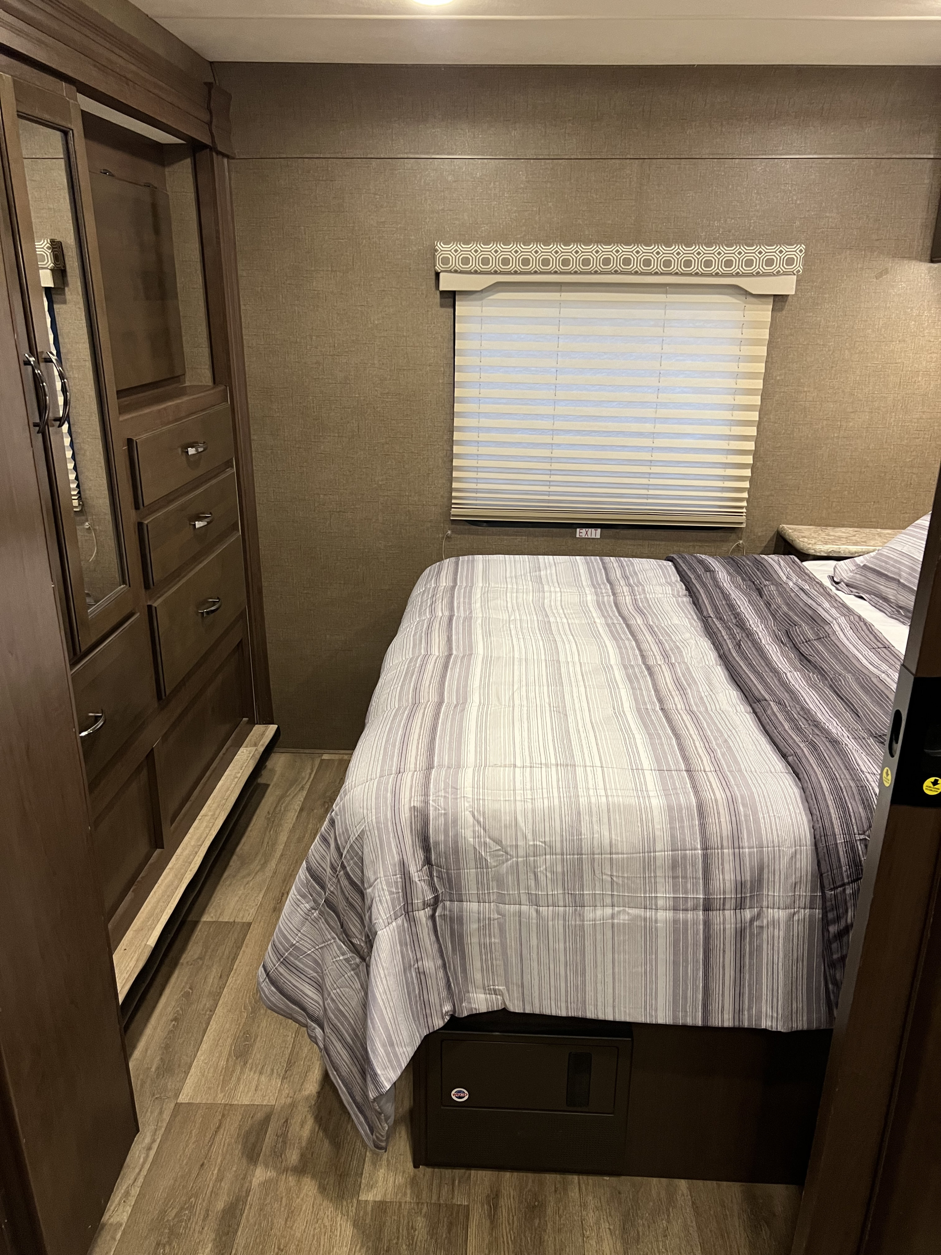 Compact RV rental bedroom featuring a striped bed, window with blinds, built-in closet, and under-bed storage/safe.. Thor Motor Coach Four Winds 2018