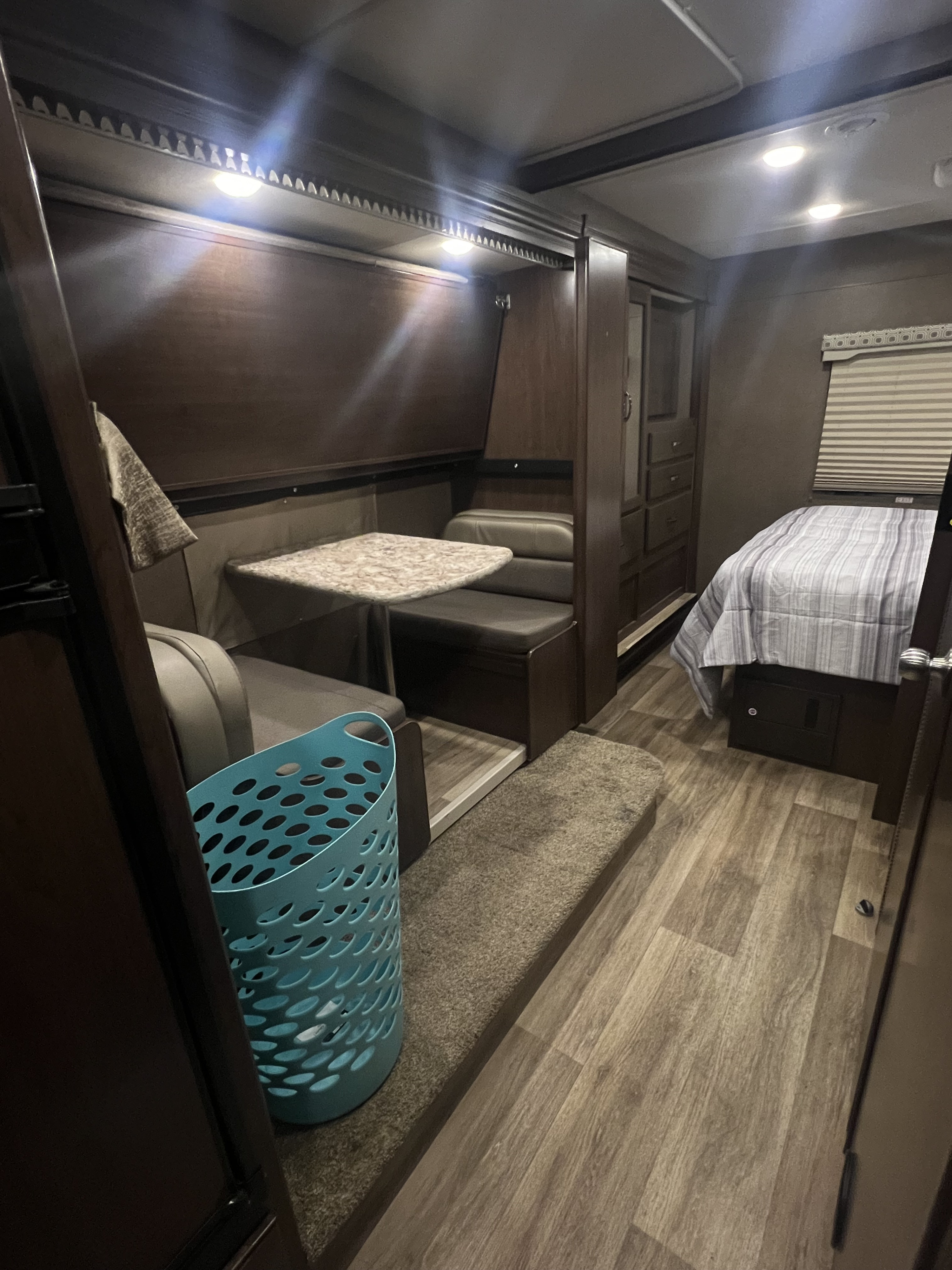 An RV rental interior featuring a dinette with bench seating, a comfortable bed, and dark wood cabinetry.. Thor Motor Coach Four Winds 2018