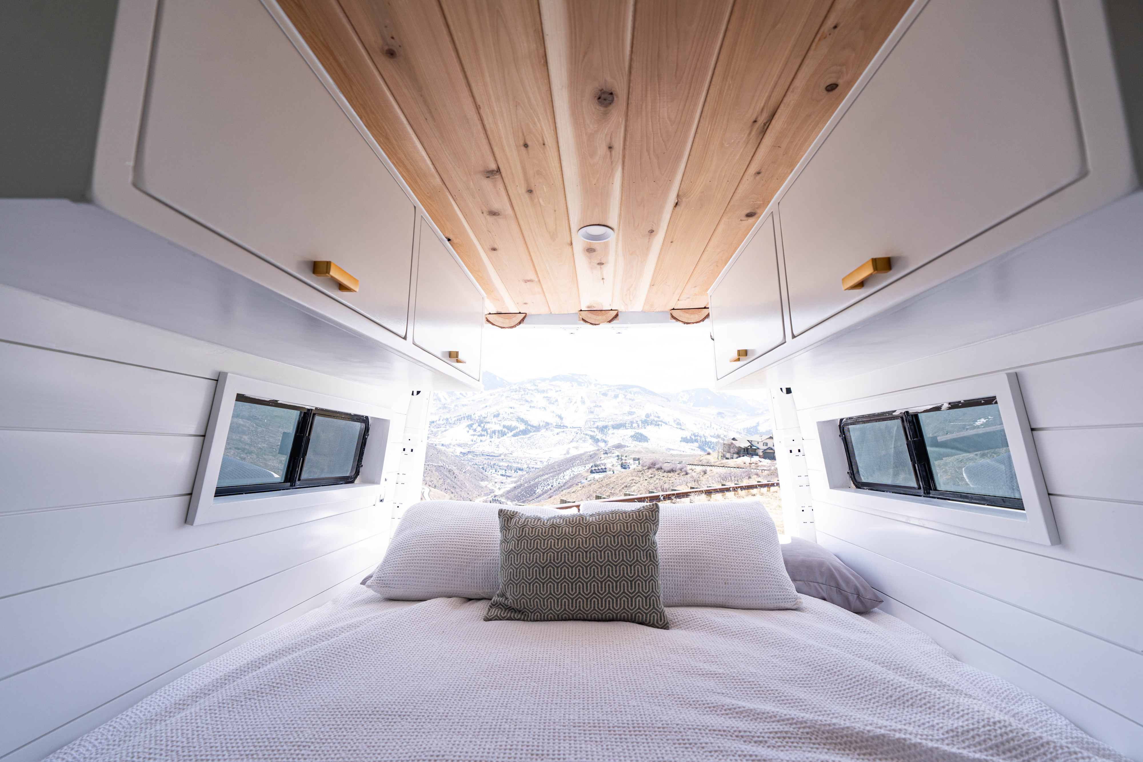 Modern RV rental: a cozy bedroom with overhead cabinets, wooden ceiling, and snowy mountain views.. Mercedes-Benz Sprinter-Loaded 2022