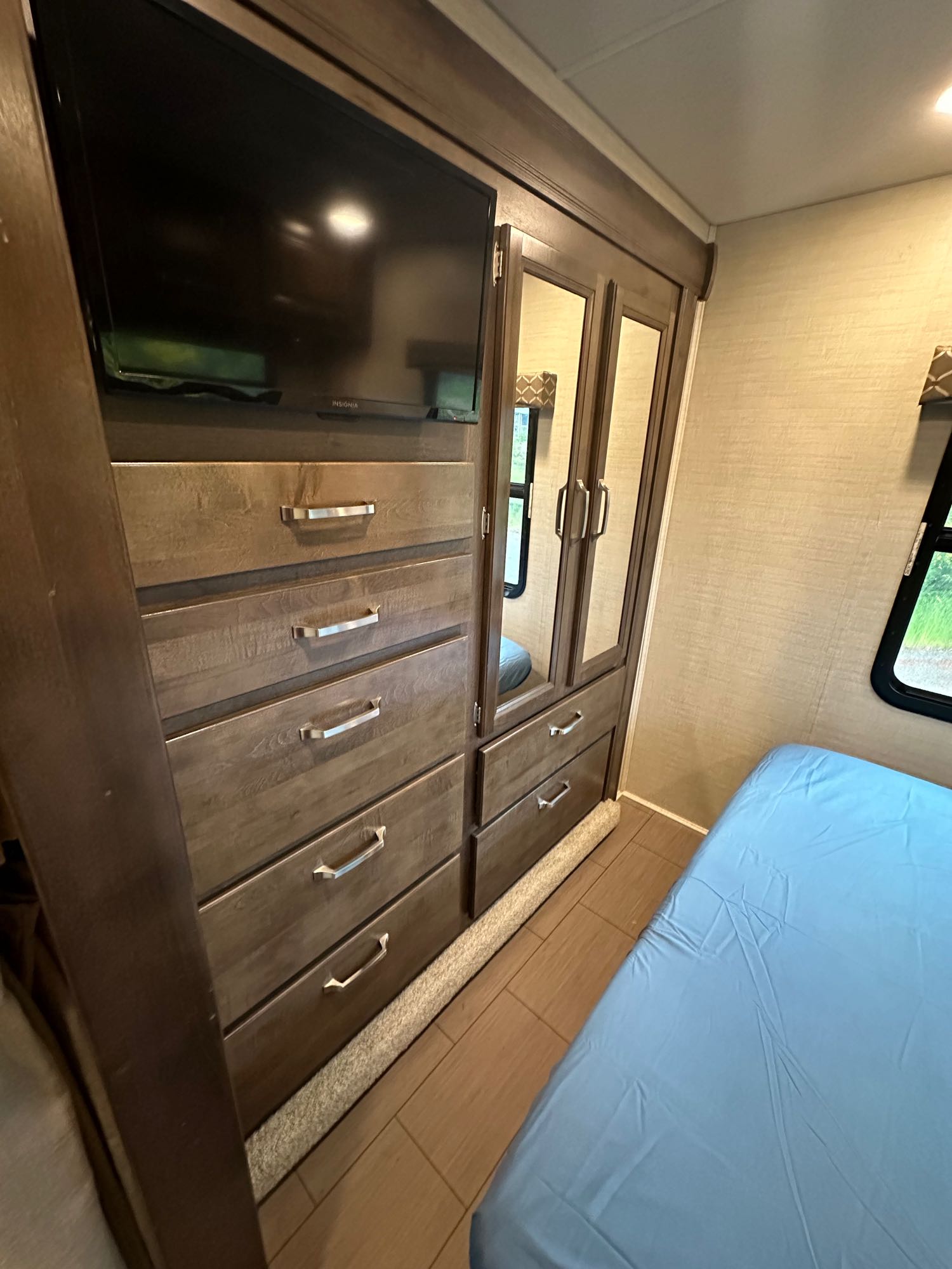 RV rental bedroom with wood dresser, TV, mirrored closet, and light blue bed.. Jayco Greyhawk 2019