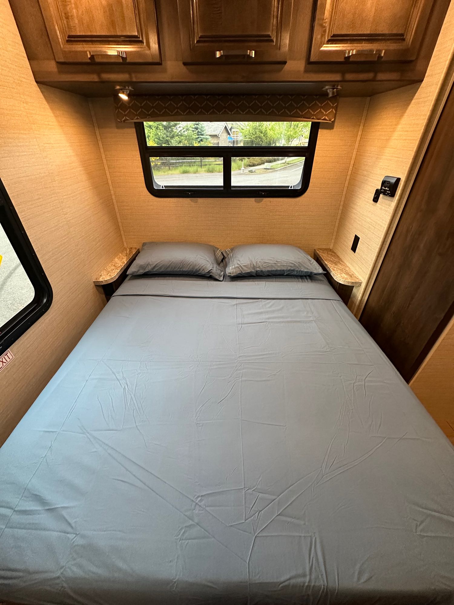 RV rental: Interior of a cozy bedroom with a bed, gray linens, overhead cabinets, and window providing natural light.. Jayco Greyhawk 2019