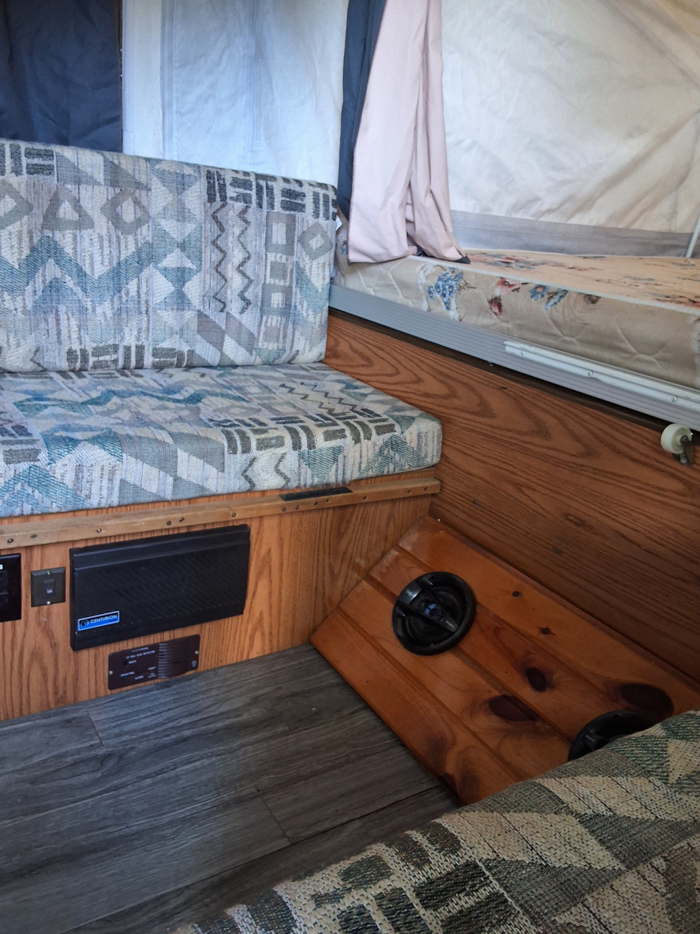 Inside an rv rental: patterned cushions, wood panels, gray flooring, and sleeping area. A compact camper interior.. Rockwood Other 2002