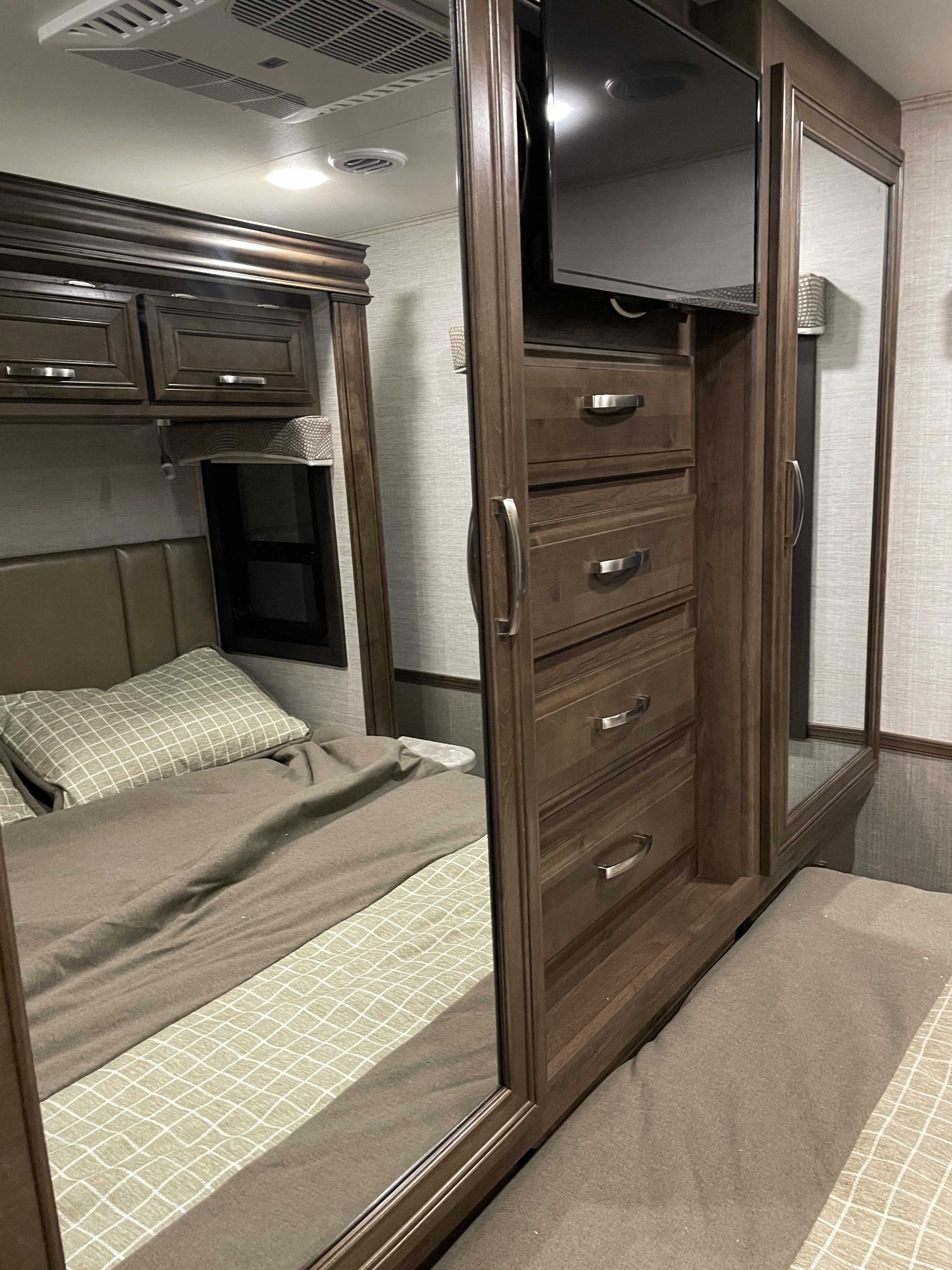 Modern RV rental bedroom interior featuring a comfy bed, overhead cabinets, and a versatile wardrobe with a TV.. Entegra Coach Vision 2021