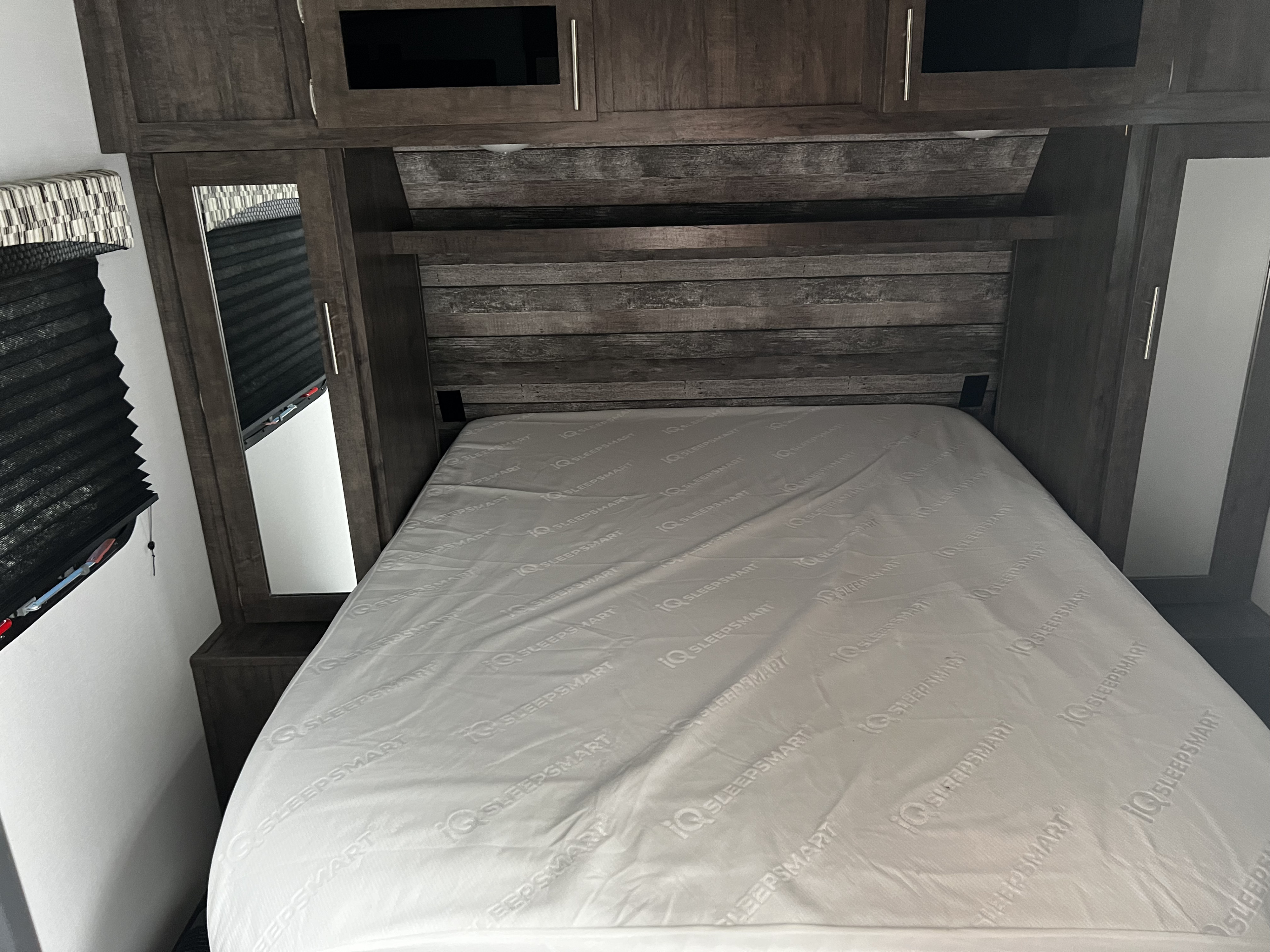 RV rental bedroom with dark wood built-ins and a white "IQ SLEEPSMART" mattress.. Riverside RV Intrepid 2021