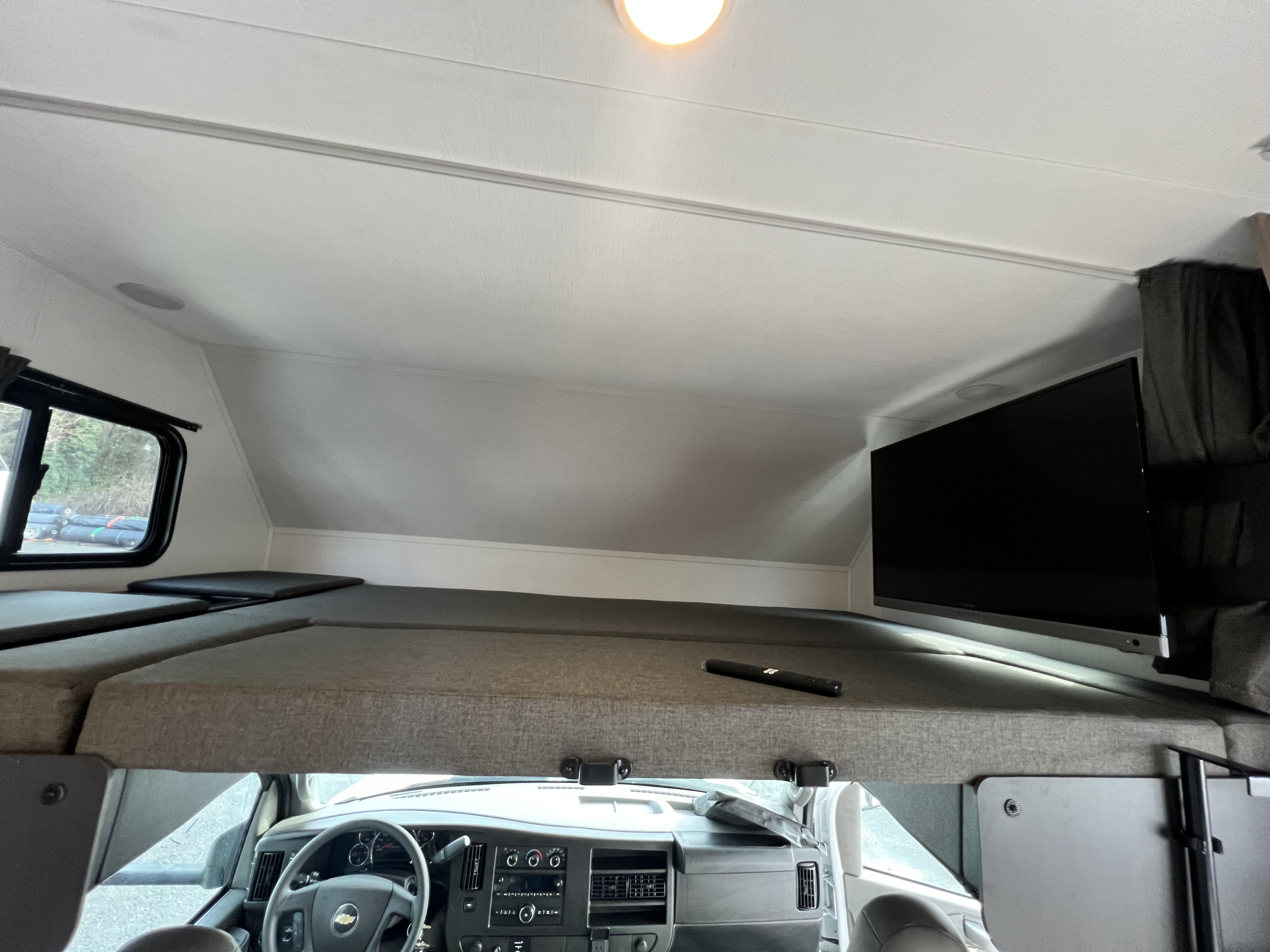 RV rental interior: Cab-over bunk with a TV, window, and the driver's cockpit visible below.. Forest River Sunseeker 2025