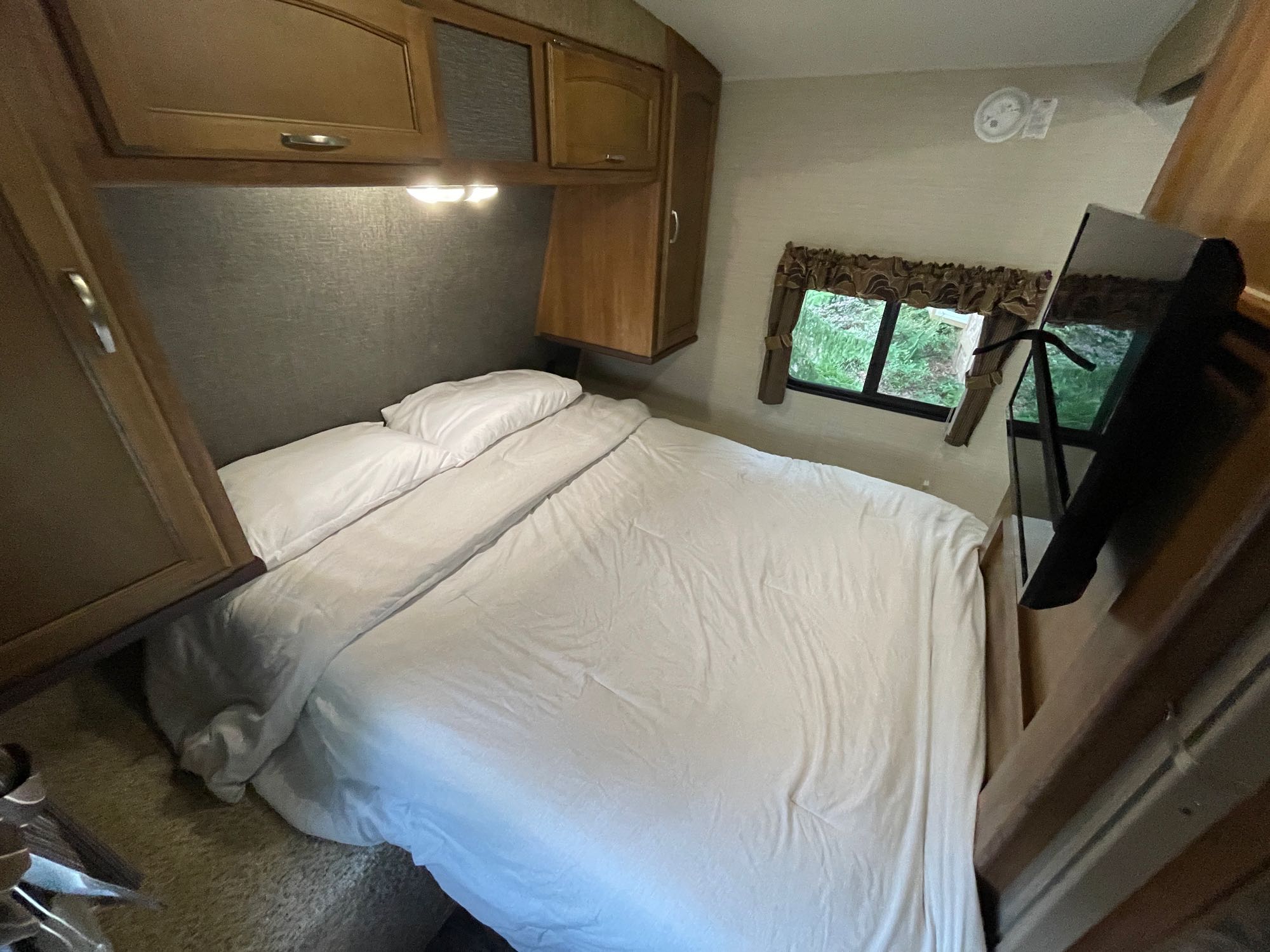 RV rental bedroom showing a cozy bed, wood cabinets, reading lights, and a window with nature views.. Keystone RV Springdale 2016