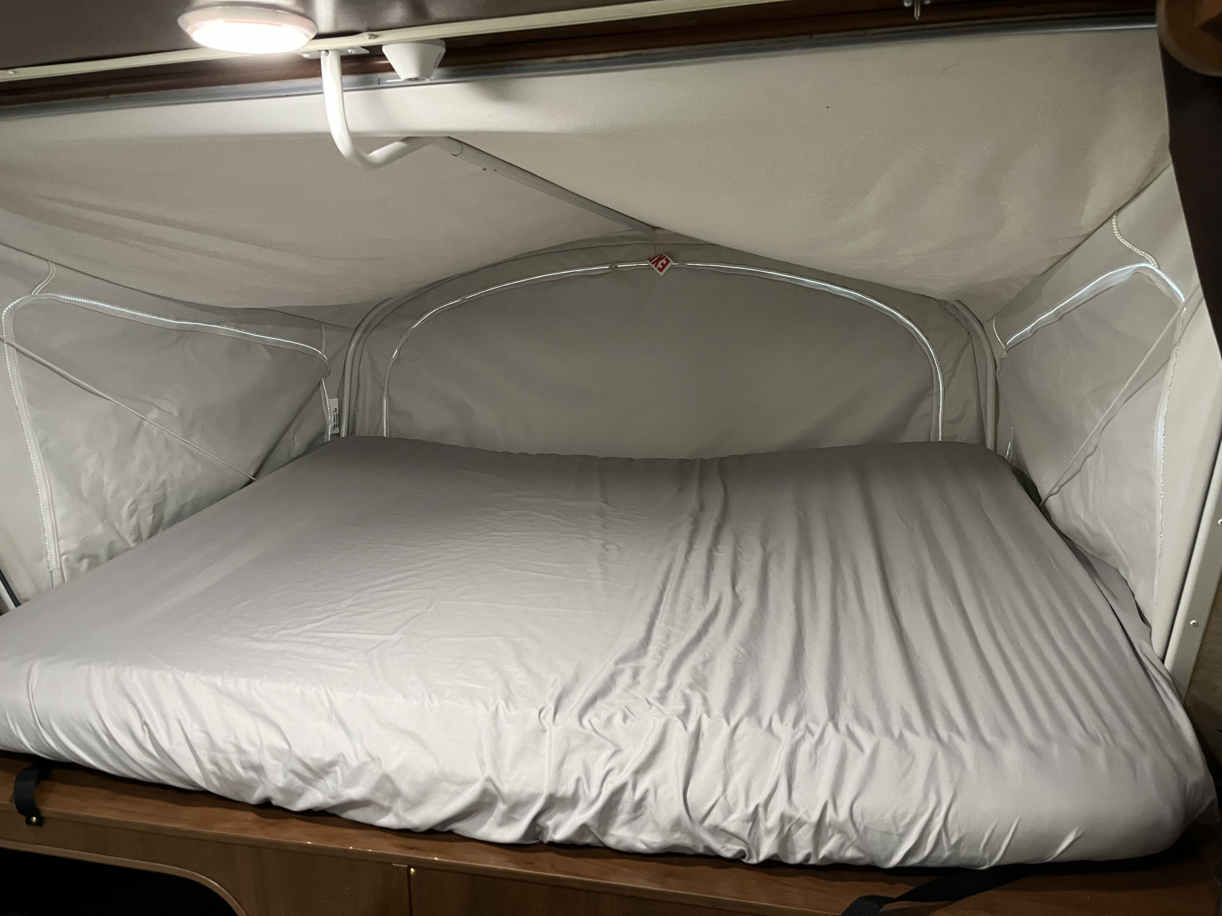 Inside a pop-up RV rental, a comfy bed with light gray sheets awaits. Perfect for your next road trip or camping adventure.. Jayco Jay Feather 2016