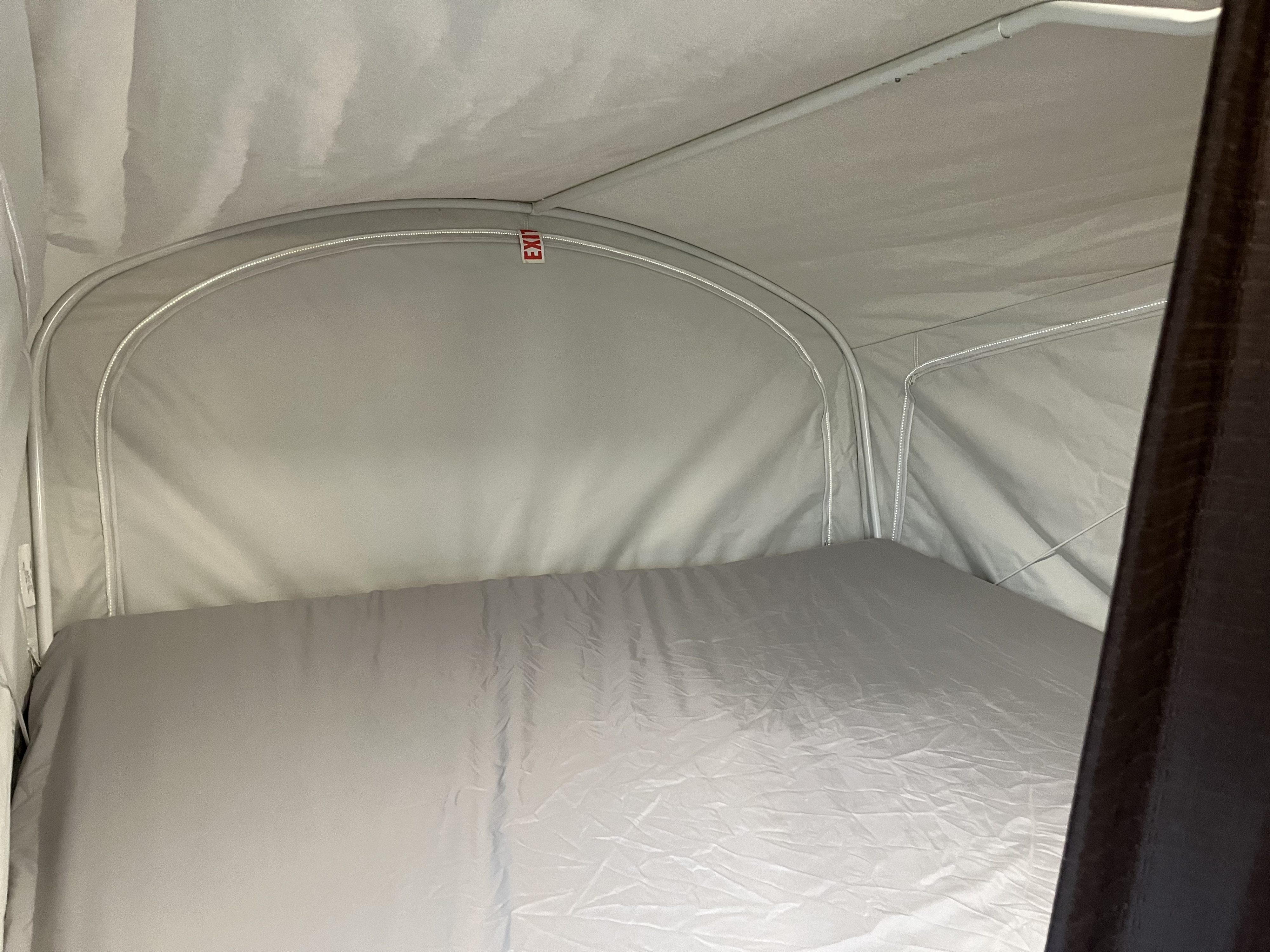 Cozy rv rental pop-up camper interior showing a light grey bed and fabric walls, with a red "EXIT" sign near the top.. Jayco Jay Feather 2016