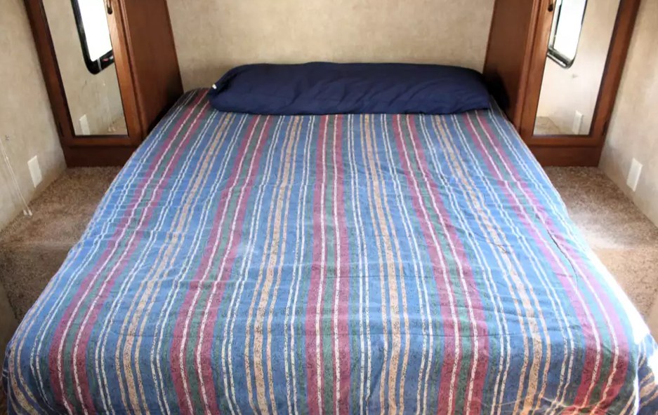 RV rental bedroom with a striped comforter, dark blue pillow, and mirrored bedside storage over carpet.. Forest River Salem Cruise Lite 2014