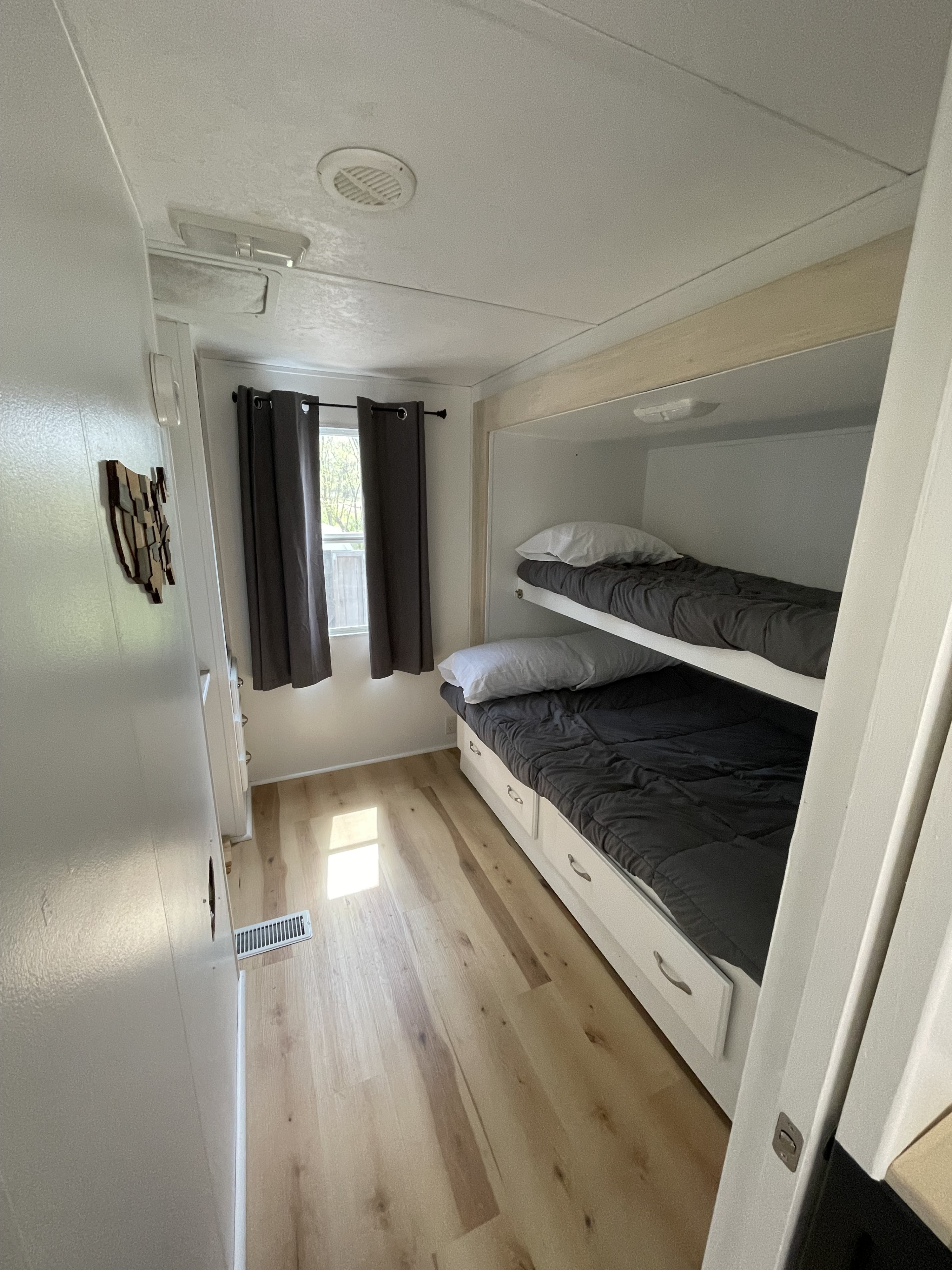 Cozy rv rental bunk beds with storage drawers & light wood floor in a compact sleeping area. Window with curtains.. Keystone RV Copper Canyon 2006