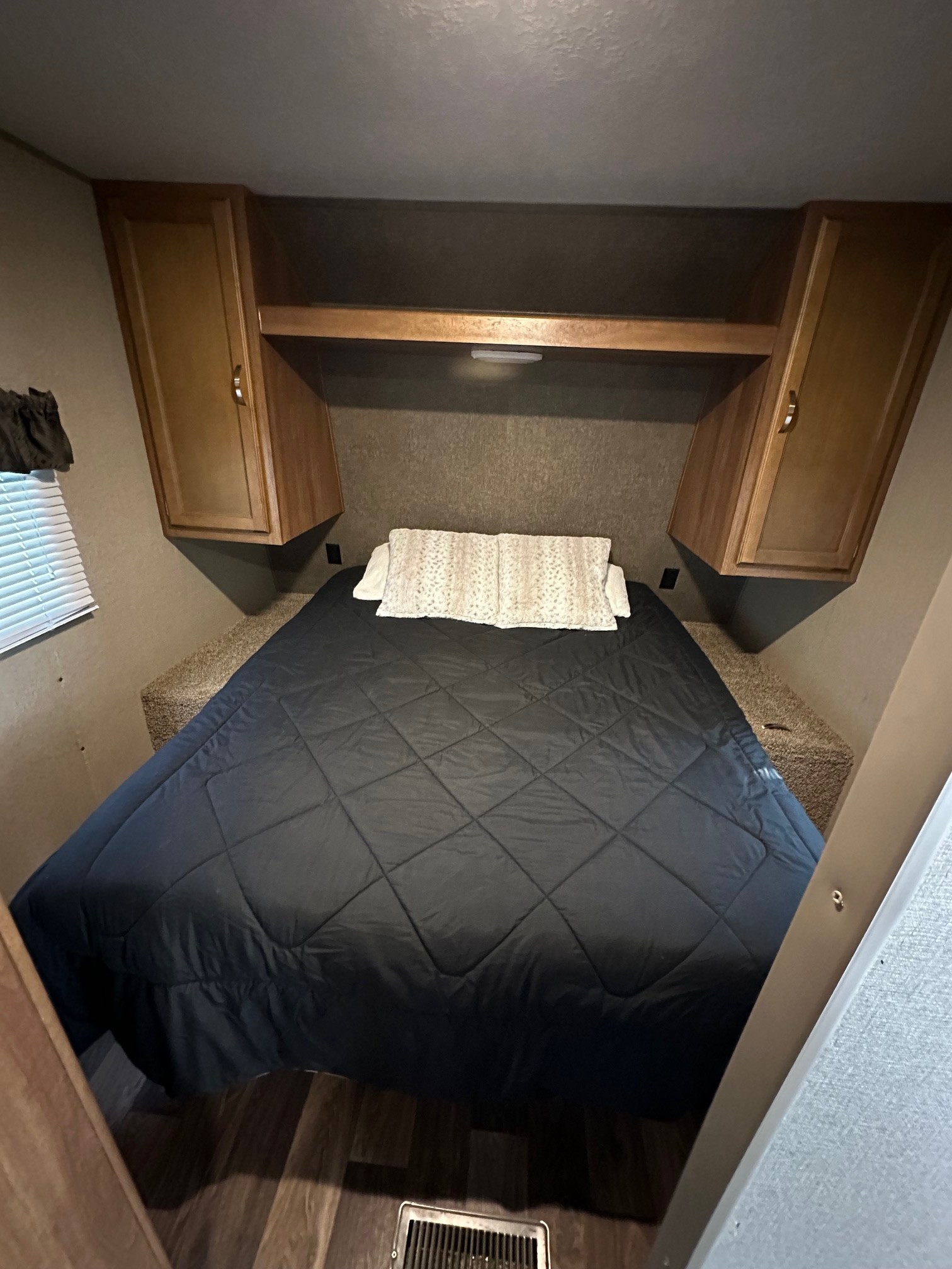 This RV rental features a cozy bedroom with a queen bed, black comforter, overhead storage, and built-in cabinetry.. Keystone RV Summerland 2017