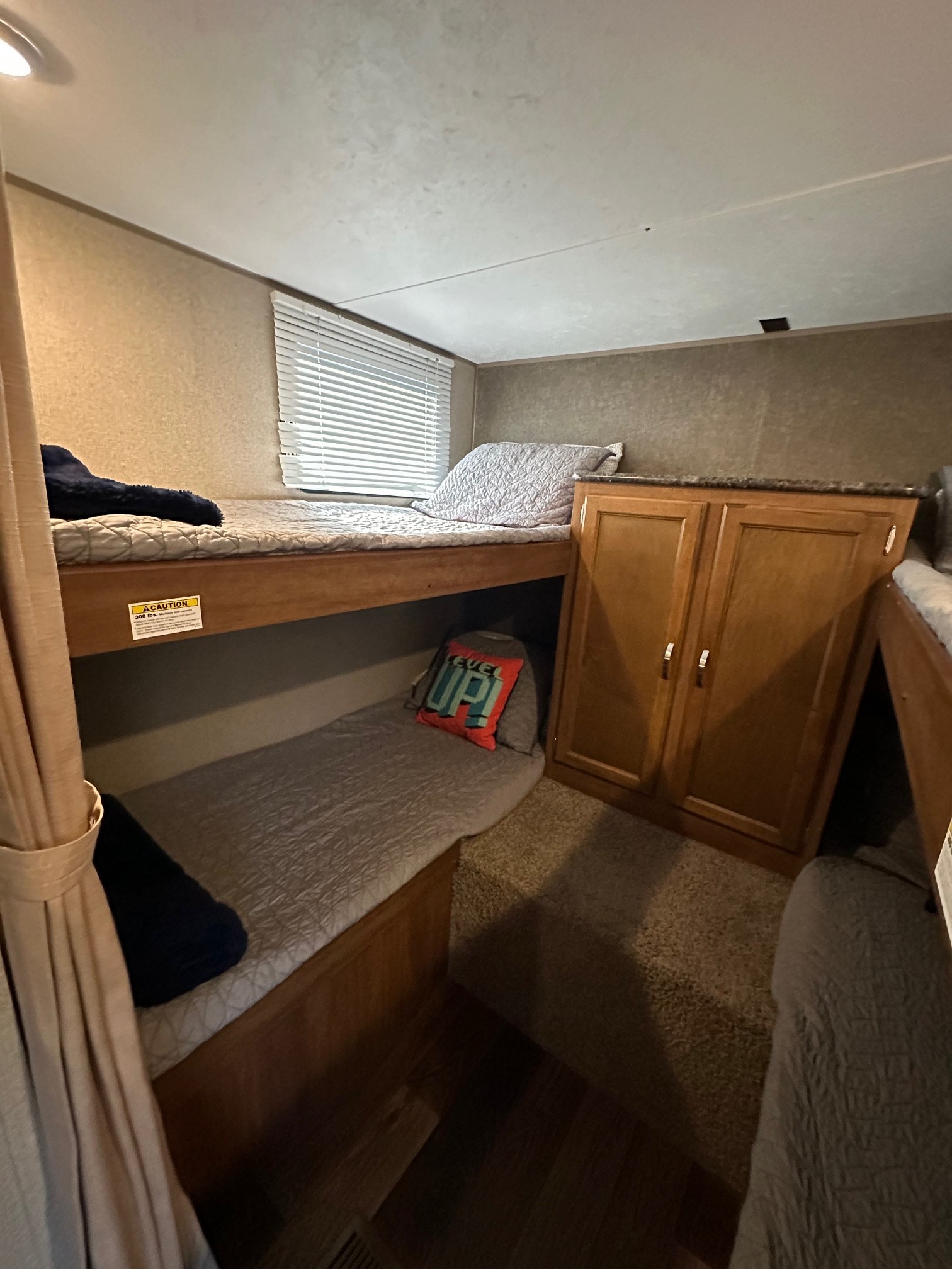 RV rental interior: bunk beds with a 300lb weight limit, window blinds, and storage cabinet. Compact sleeping space.. Keystone RV Summerland 2017