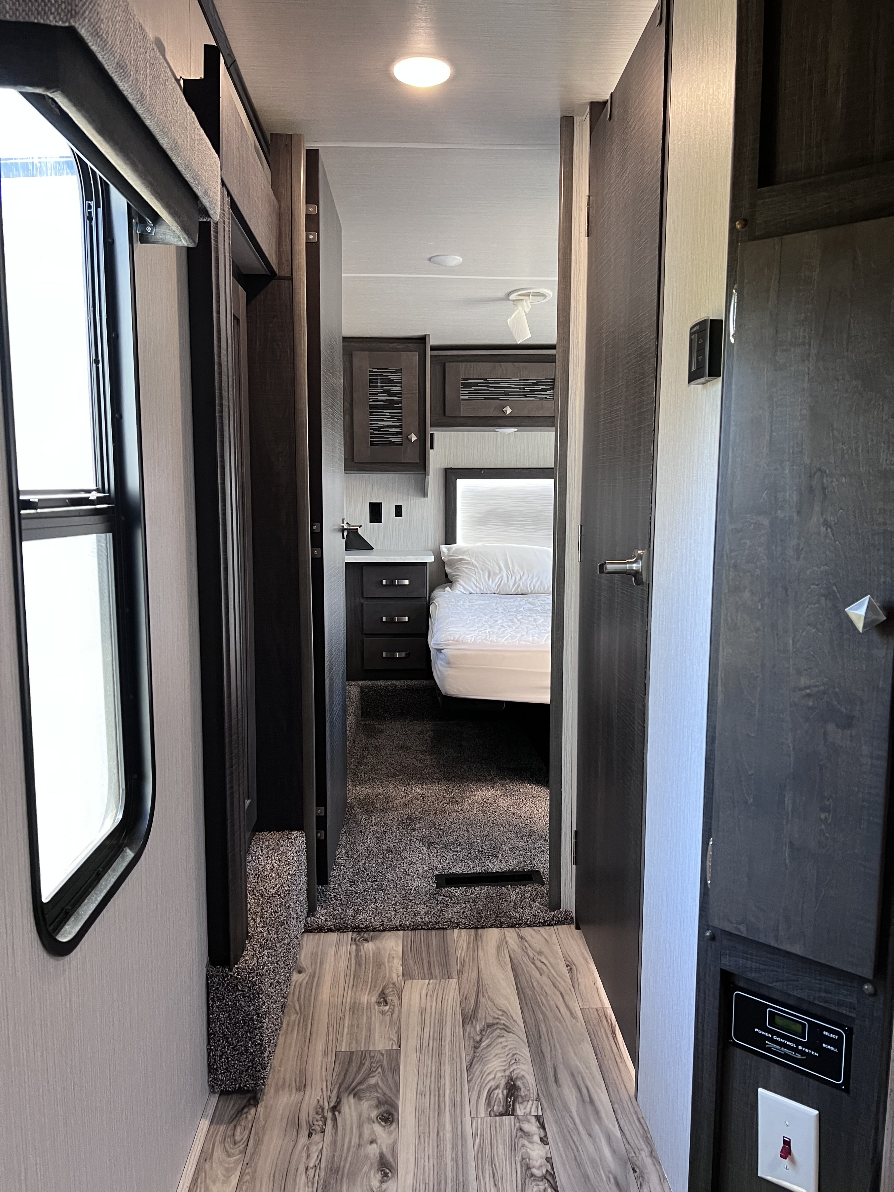 Inside this RV rental, view down a hallway to a comfortable bedroom area with modern furnishings and controls.. Heartland RVs Road Warrior Toy Hauler 2021
