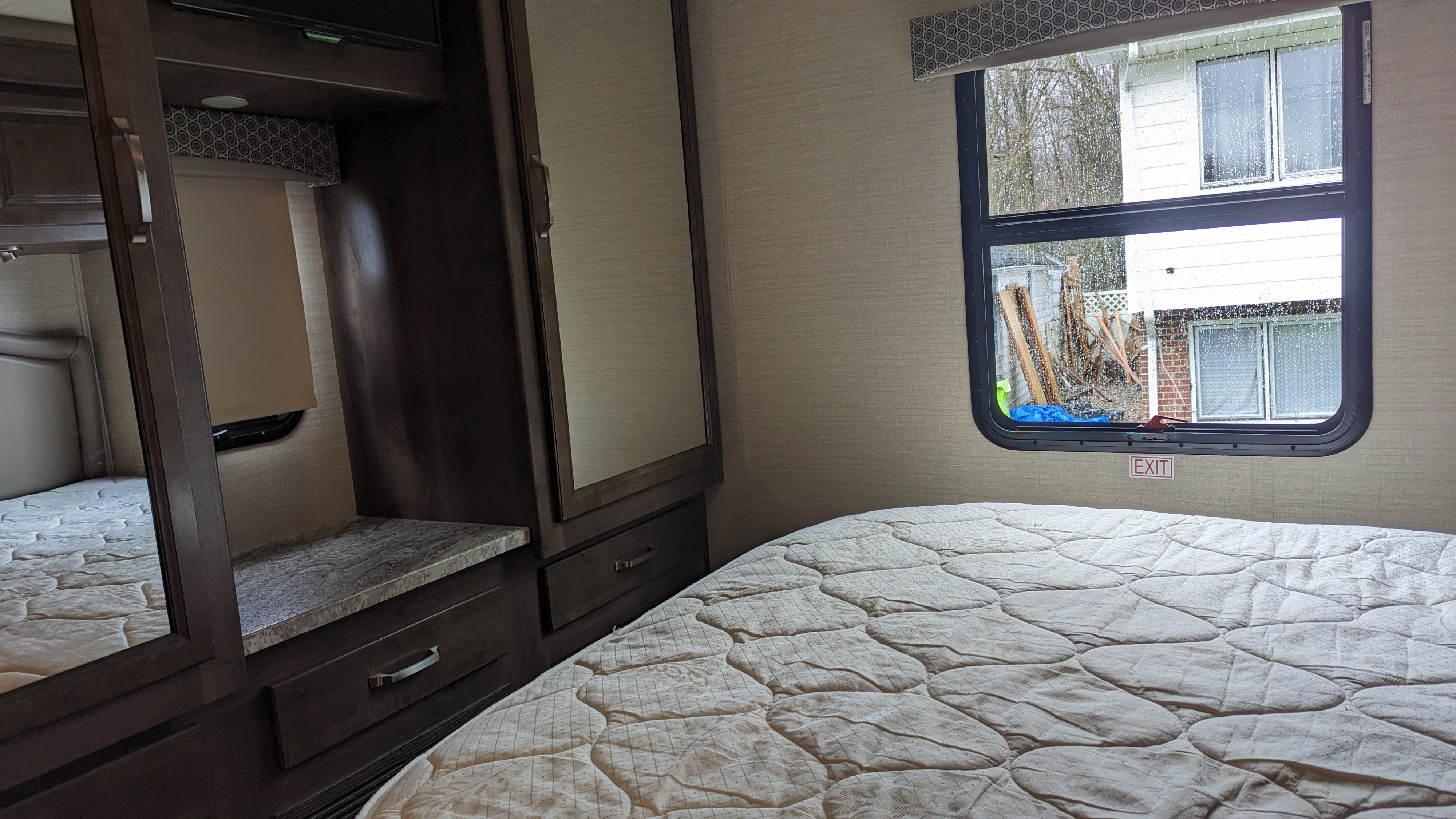 Cozy RV rental bedroom with a comfy bed, mirrored wardrobe, and a window view of a rainy day.. Jayco Greyhawk 2019