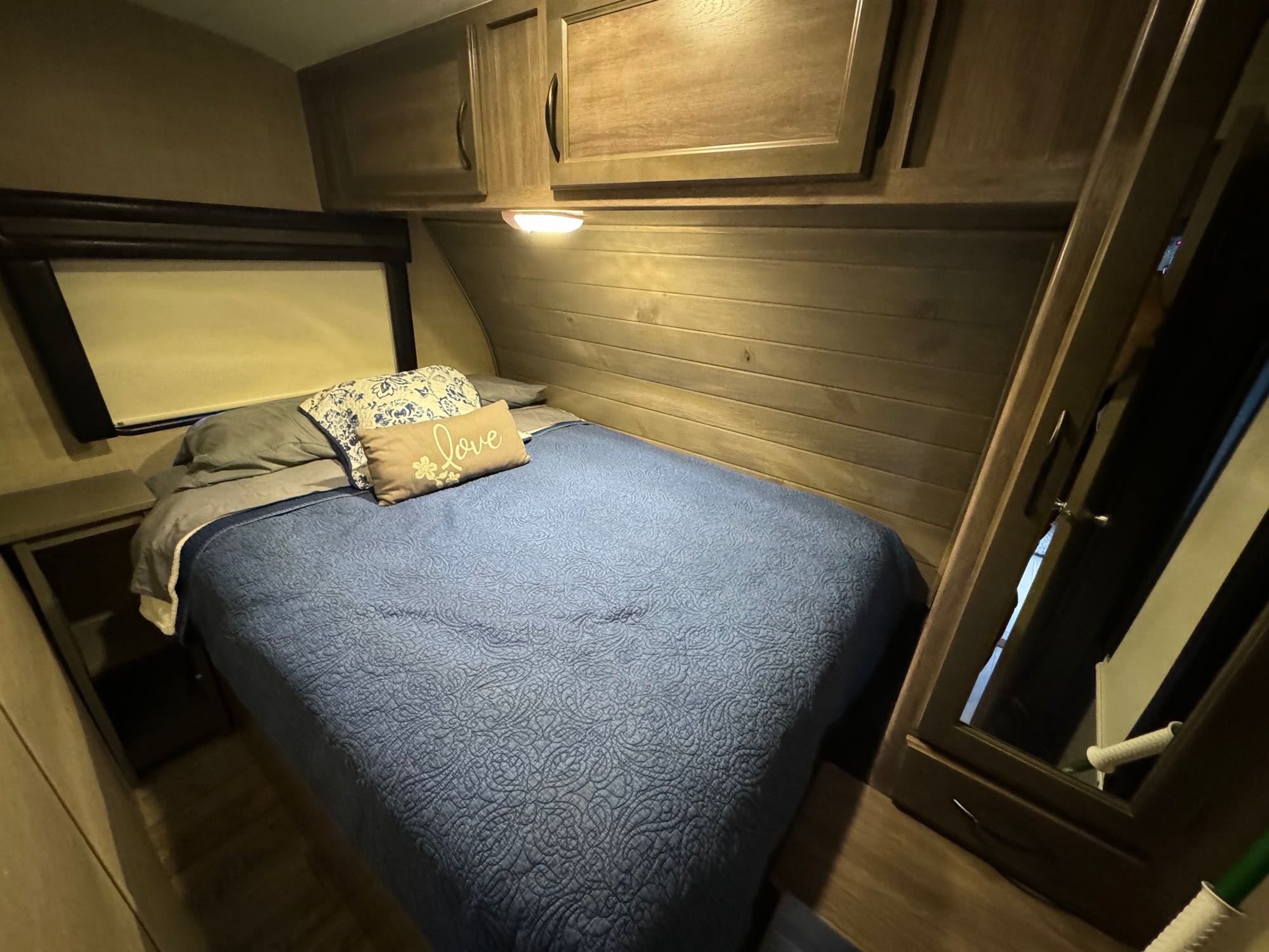 Inside an RV rental: a compact bedroom with a blue bed, cabinets, and mirror, offering a comfortable stay.. Pacific Coachworks Blaze'N 2017