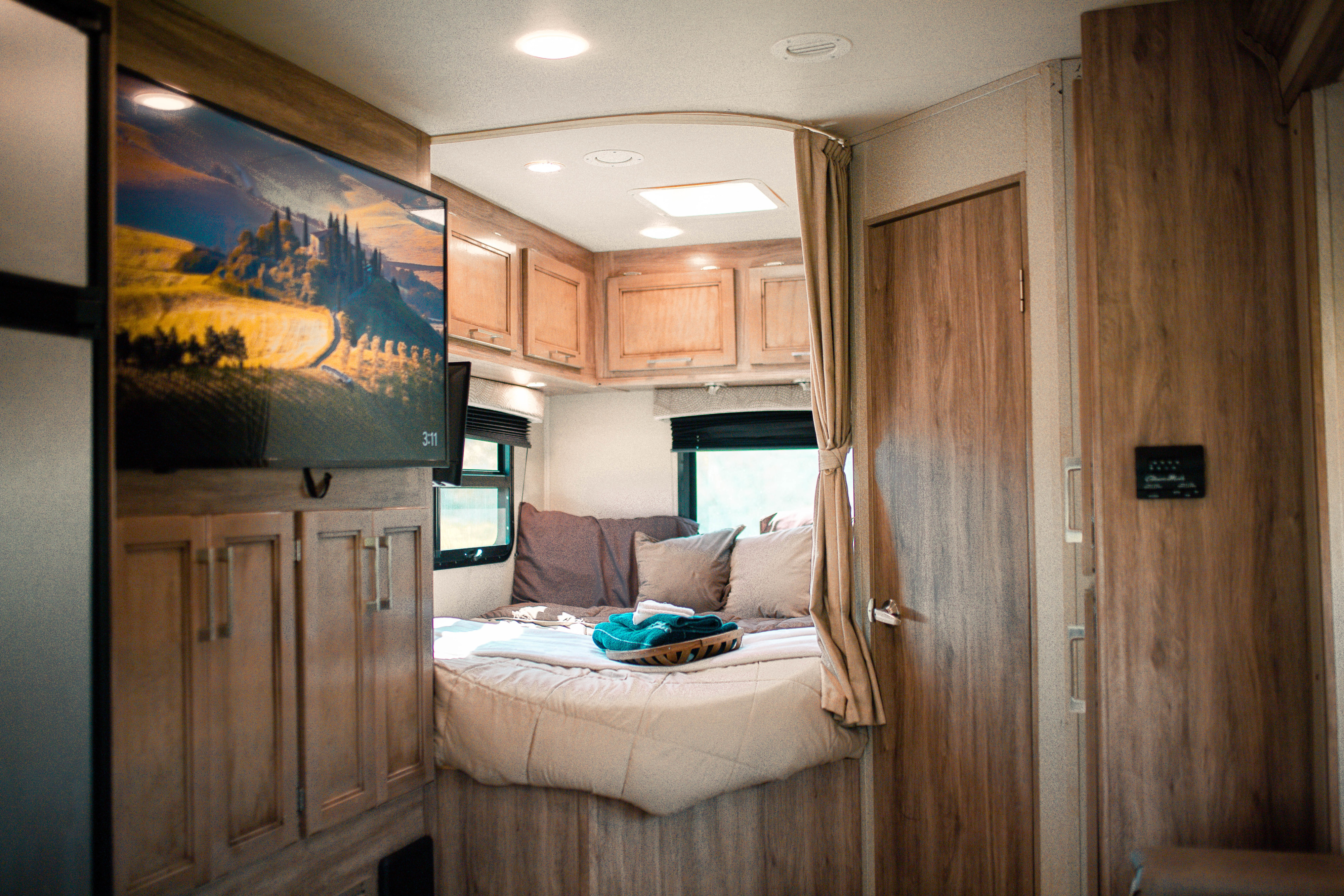 Cozy RV rental bedroom features a mounted TV, comfortable bed with fresh linens, and warm wooden interior.. Entegra Coach Odyssey 2019