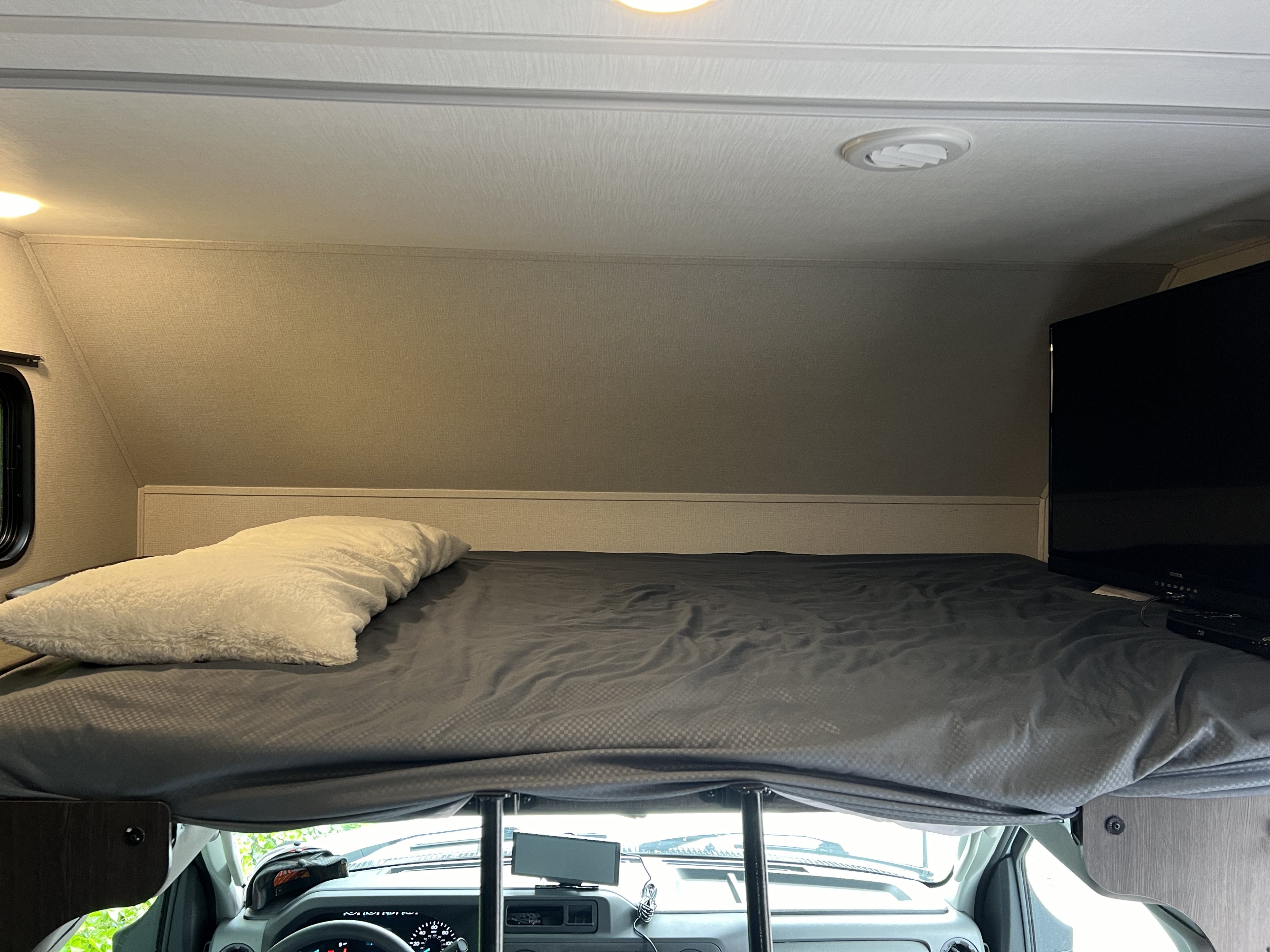 RV rental interior: A comfortable cab-over bunk bed with a white pillow and TV, situated above the vehicle's cabin.. Forester LE 2023