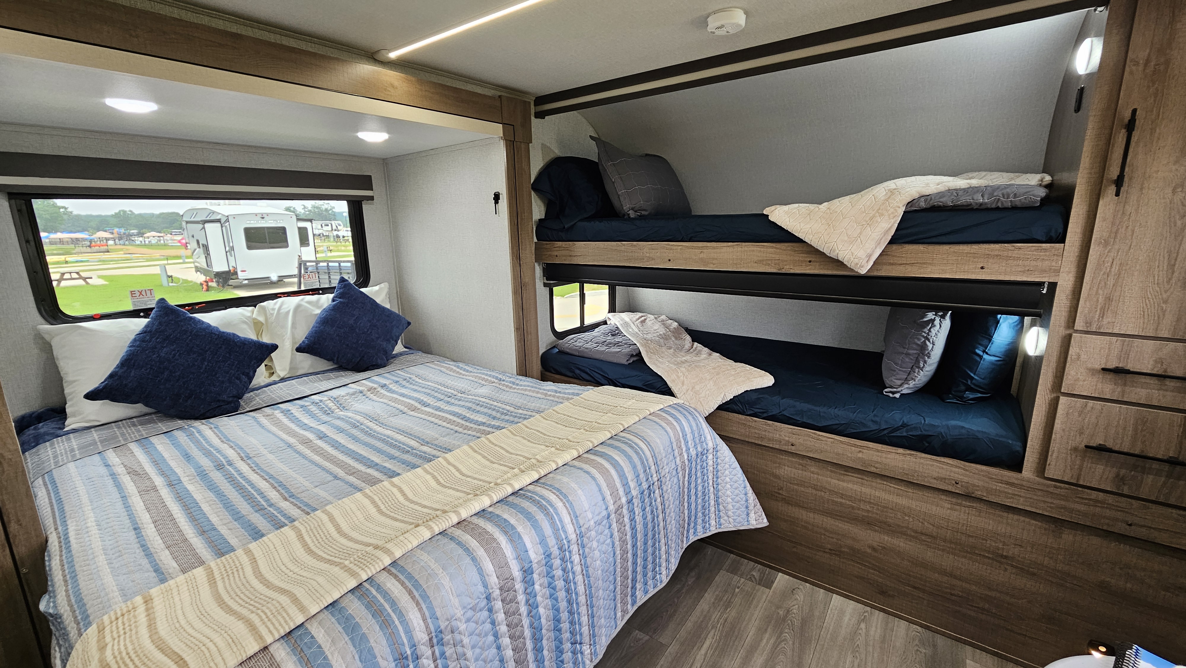 This RV rental offers a cozy main bed with blue bedding and stacked bunk beds, providing comfortable travel accommodations.. Grand Design Imagine AIM 2024