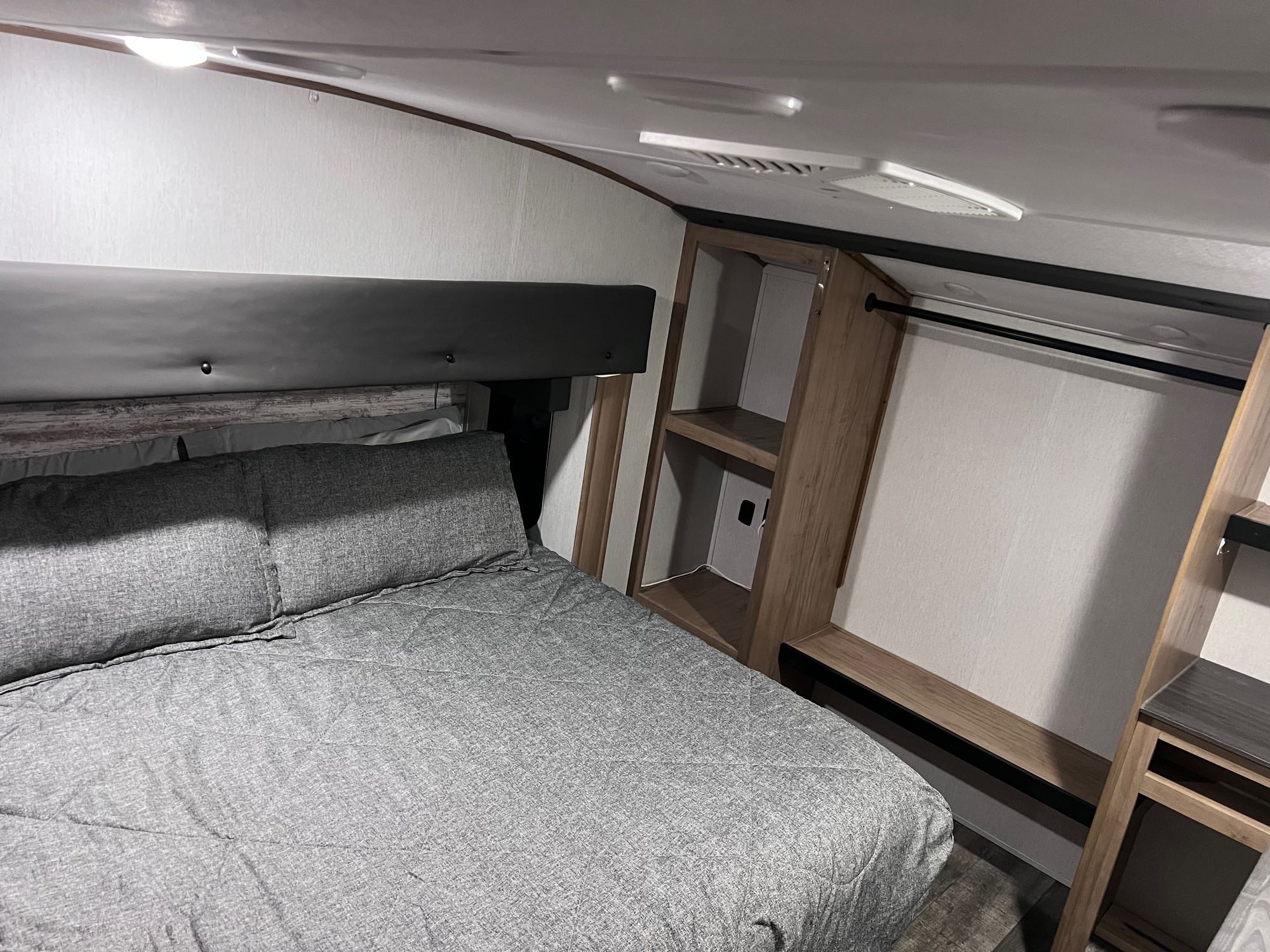 Cozy RV rental bedroom featuring a gray bed, built-in storage, and bright lighting, ideal for compact living.. Forest River Cherokee Arctic Wolf 2023