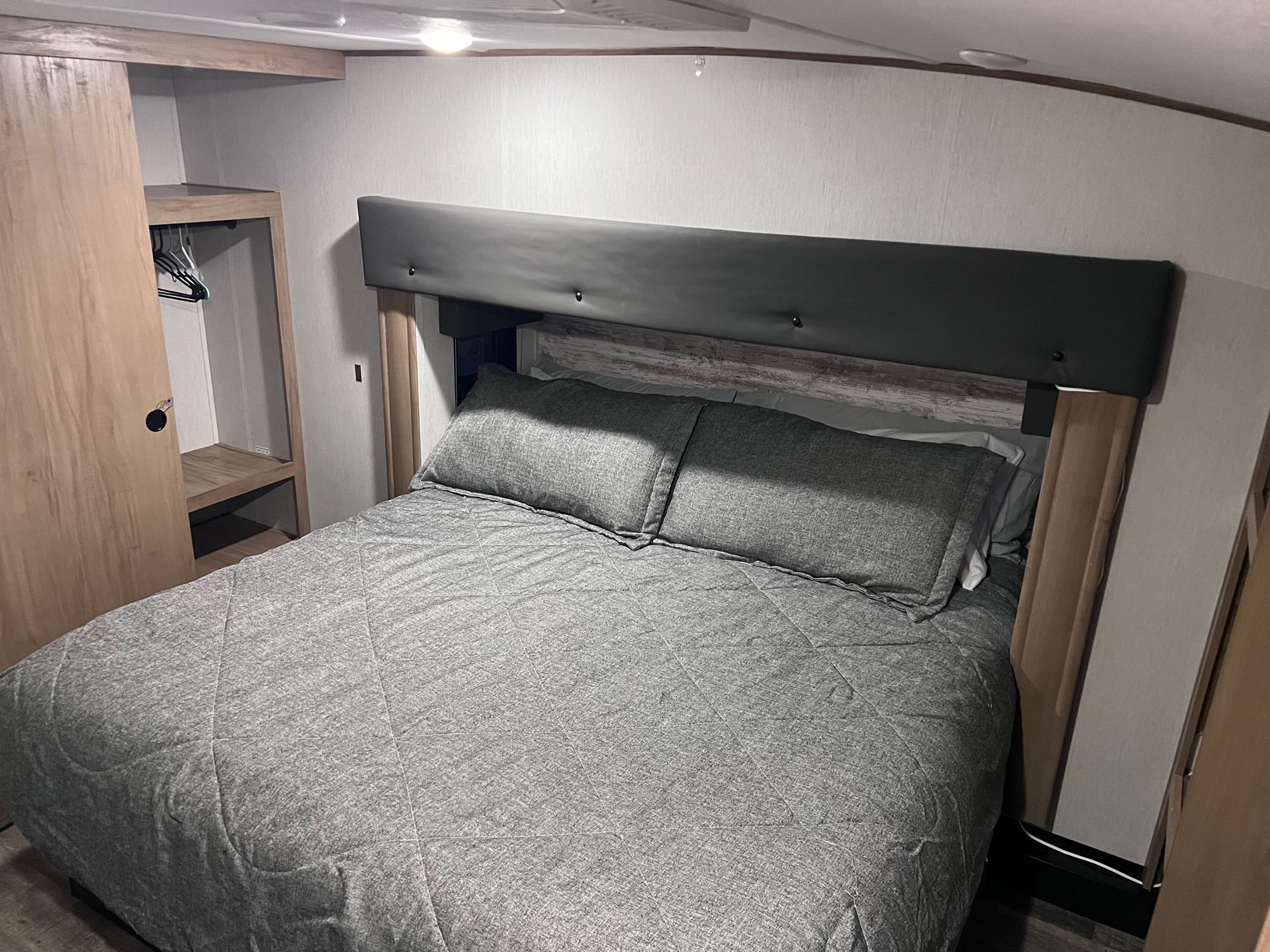 Cozy RV rental bedroom featuring a gray bed, dark headboard, and built-in wood closet.. Forest River Cherokee Arctic Wolf 2023
