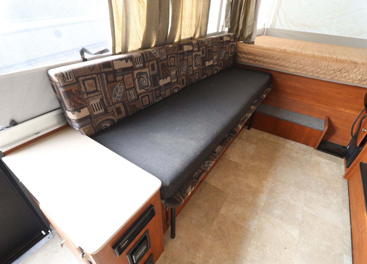 RV rental interior showing a long patterned dinette, a small counter, and a bed in the background.. Somerset Somerset Popup Trailer 2019