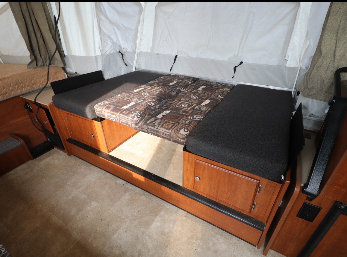 RV rental's versatile interior with a convertible dinette and bed, featuring dark cushions and wood storage units.. Somerset Somerset Popup Trailer 2019