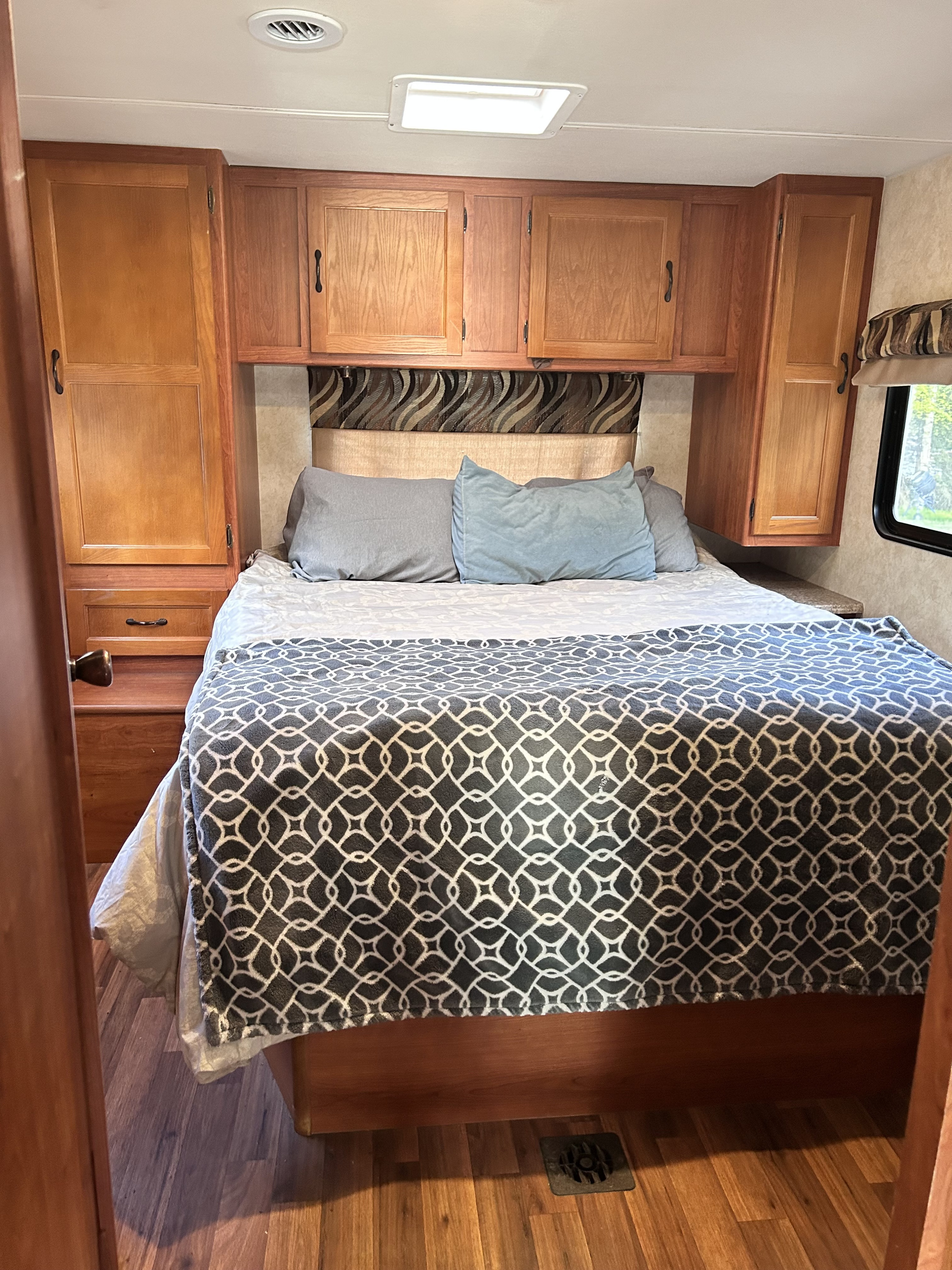 Cozy RV rental bedroom interior featuring a comfortable bed, wooden overhead cabinets for storage, and a window for natural light.. Forest River Coachmen Freelander 2013