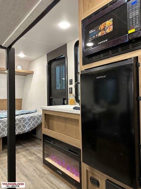 Modern RV rental interior: bedroom area on left, kitchen with microwave, fridge, and electric fireplace on right.. Forest River Cherokee Wolf Den 2024