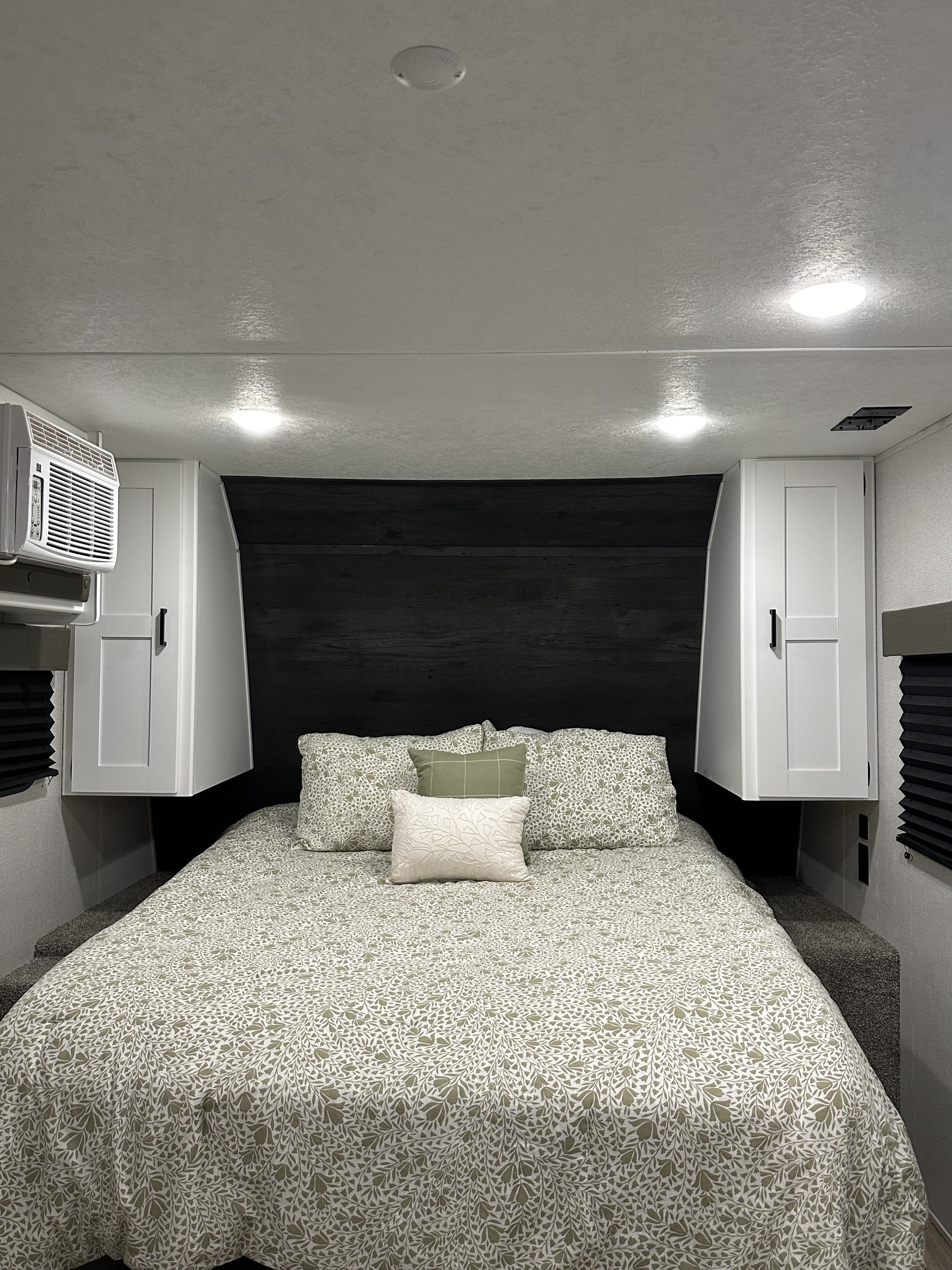 Experience comfort in this RV rental bedroom: light green patterned bed, dark wood headboard, white cabinets & AC unit.. Keystone Hideout 2021