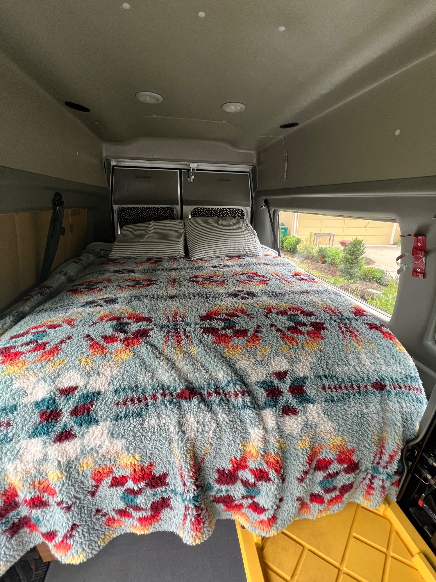 This RV rental bed features a vibrant, plush blanket and striped pillows, inviting a cozy rest in the van's interior.. Ford Econoline 150 2006