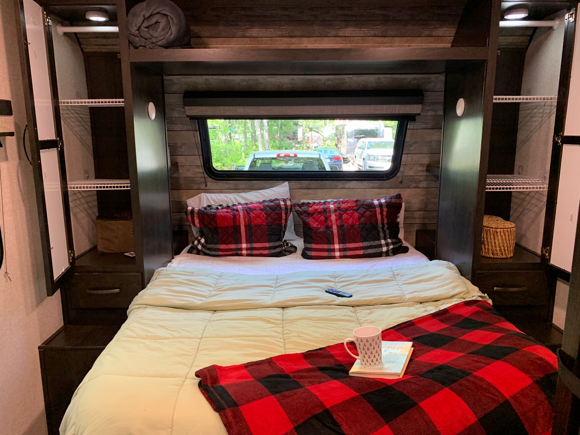 Step into comfort! This RV rental bedroom offers a cozy bed, plaid accents, ample storage, and a scenic window view.. Forest River Surveyor Legend 2020