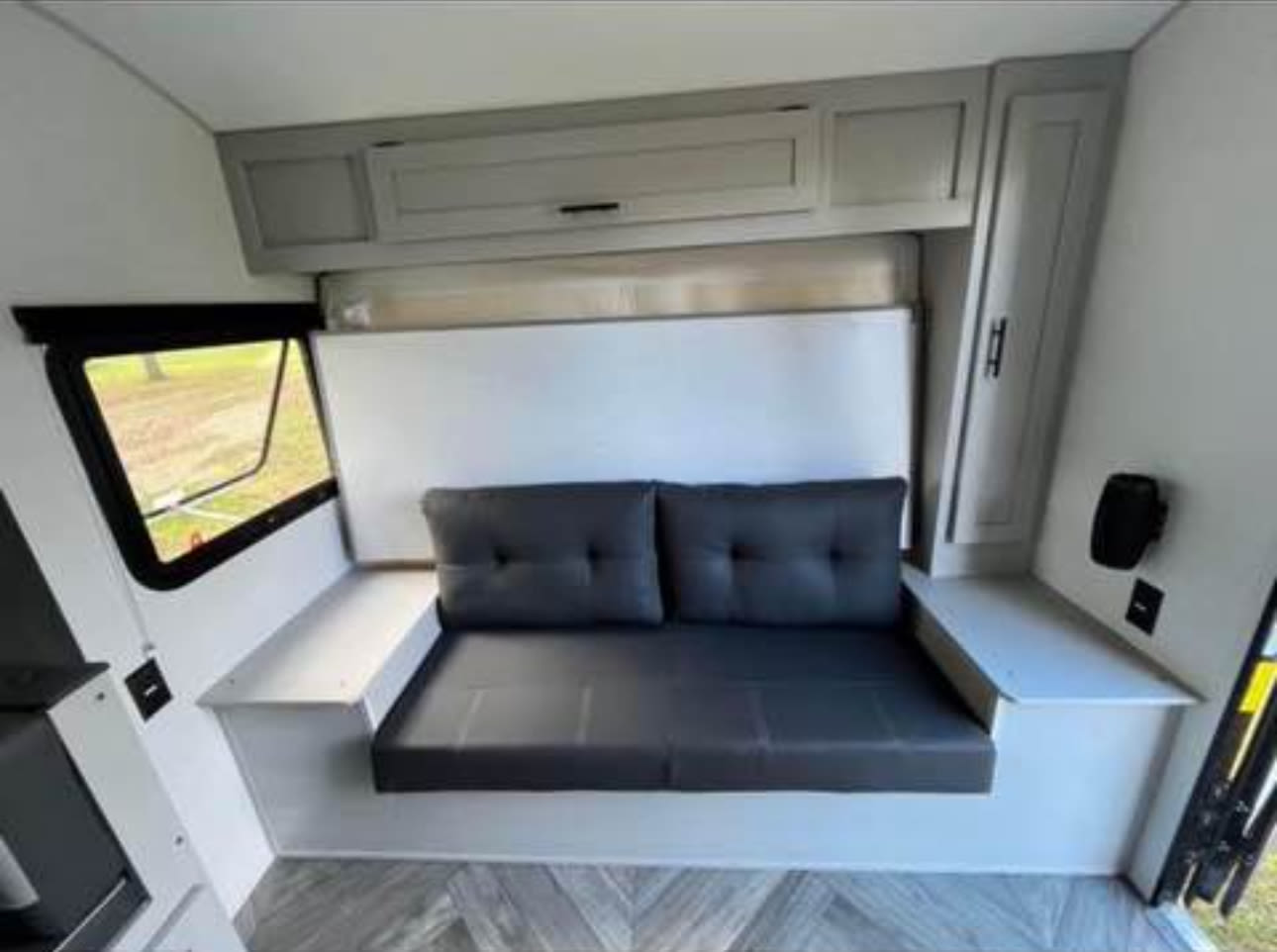 RV rental: Compact interior with a grey convertible sofa/bed, overhead cabinets, and a side window for views.. Forest River Wildwood FSX 2023
