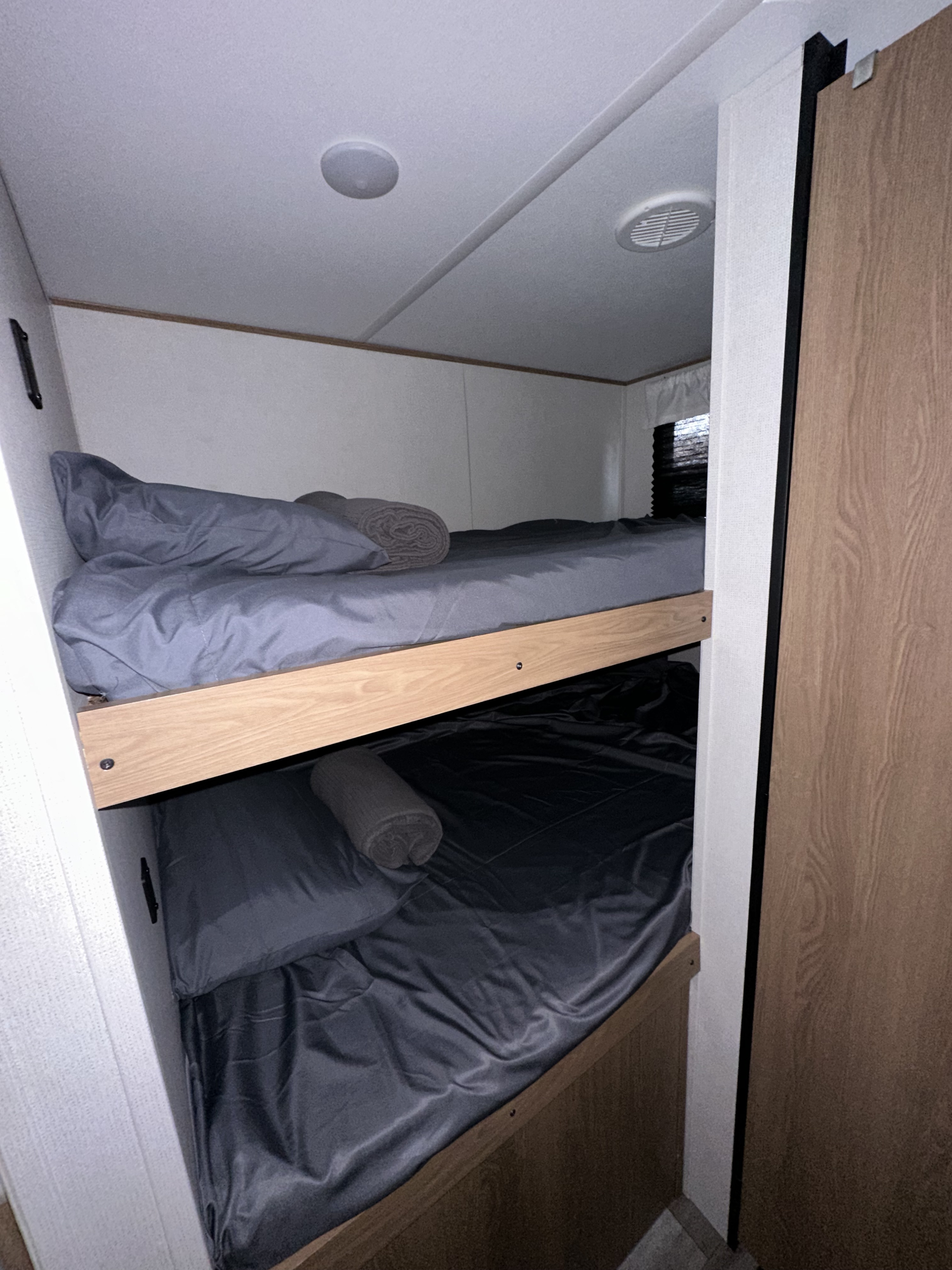 RV rental bunk beds: cozy sleeping area with gray linens, light wood frame, and window.. Forest River Explore Avenger 26BK 2023
