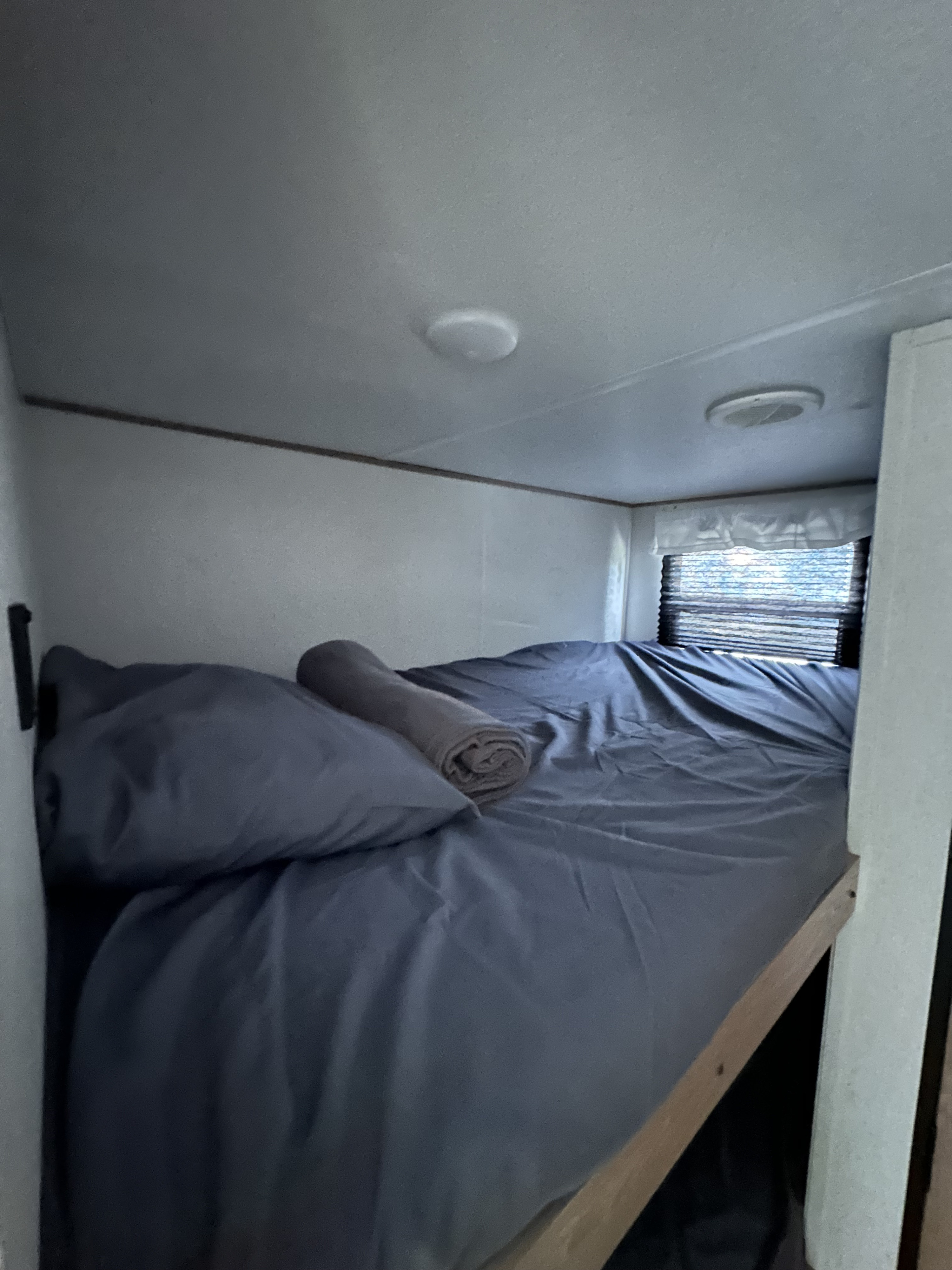 RV rental bunk bed with gray bedding, pillow, and rolled towel, providing a compact sleeping area inside.. Forest River Explore Avenger 26BK 2023