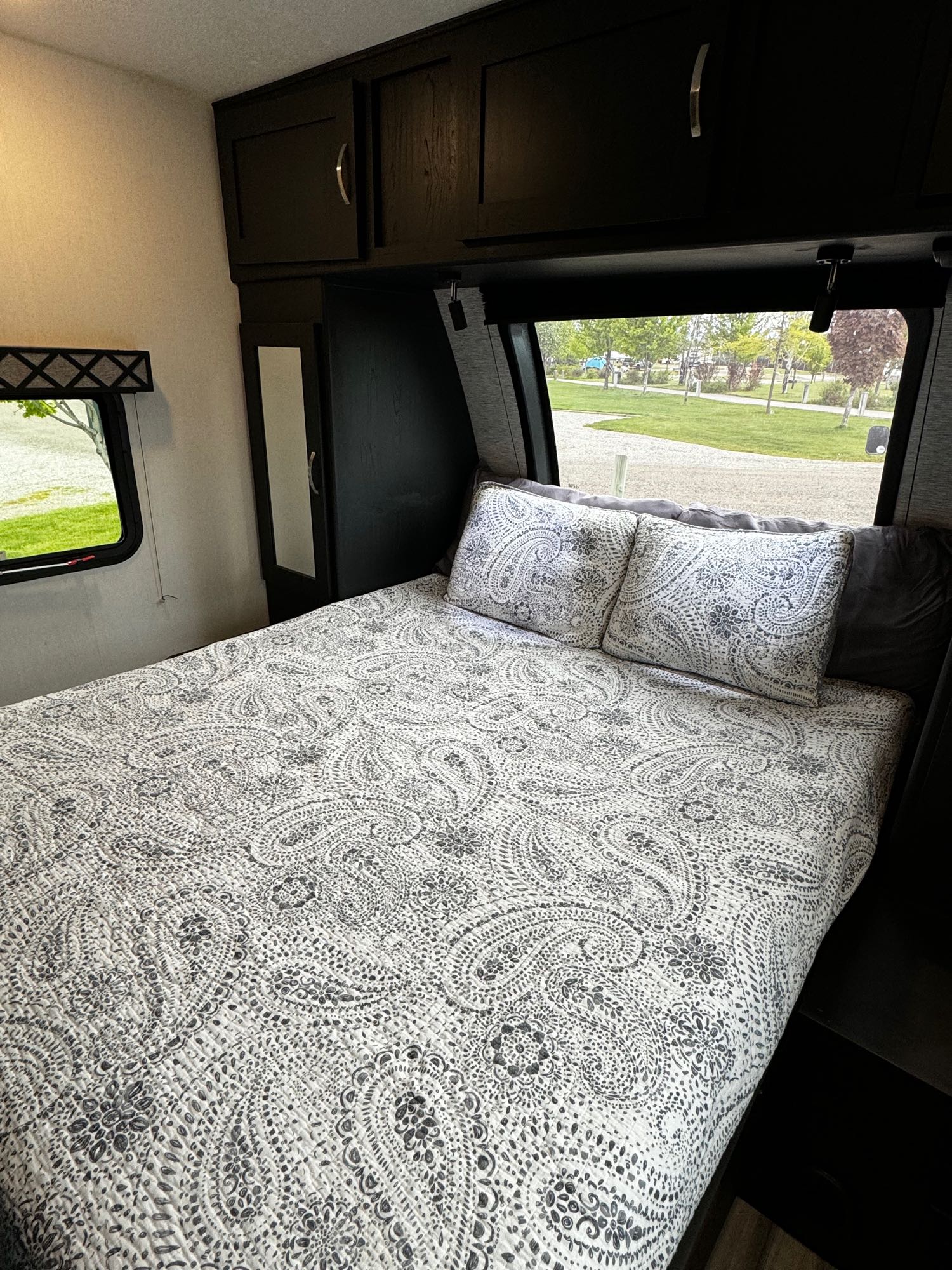 Cozy RV rental bedroom featuring a patterned comforter, overhead storage, and scenic windows with a green view.. Forest River Coachmen Freedom Express Ultra Lite 2022