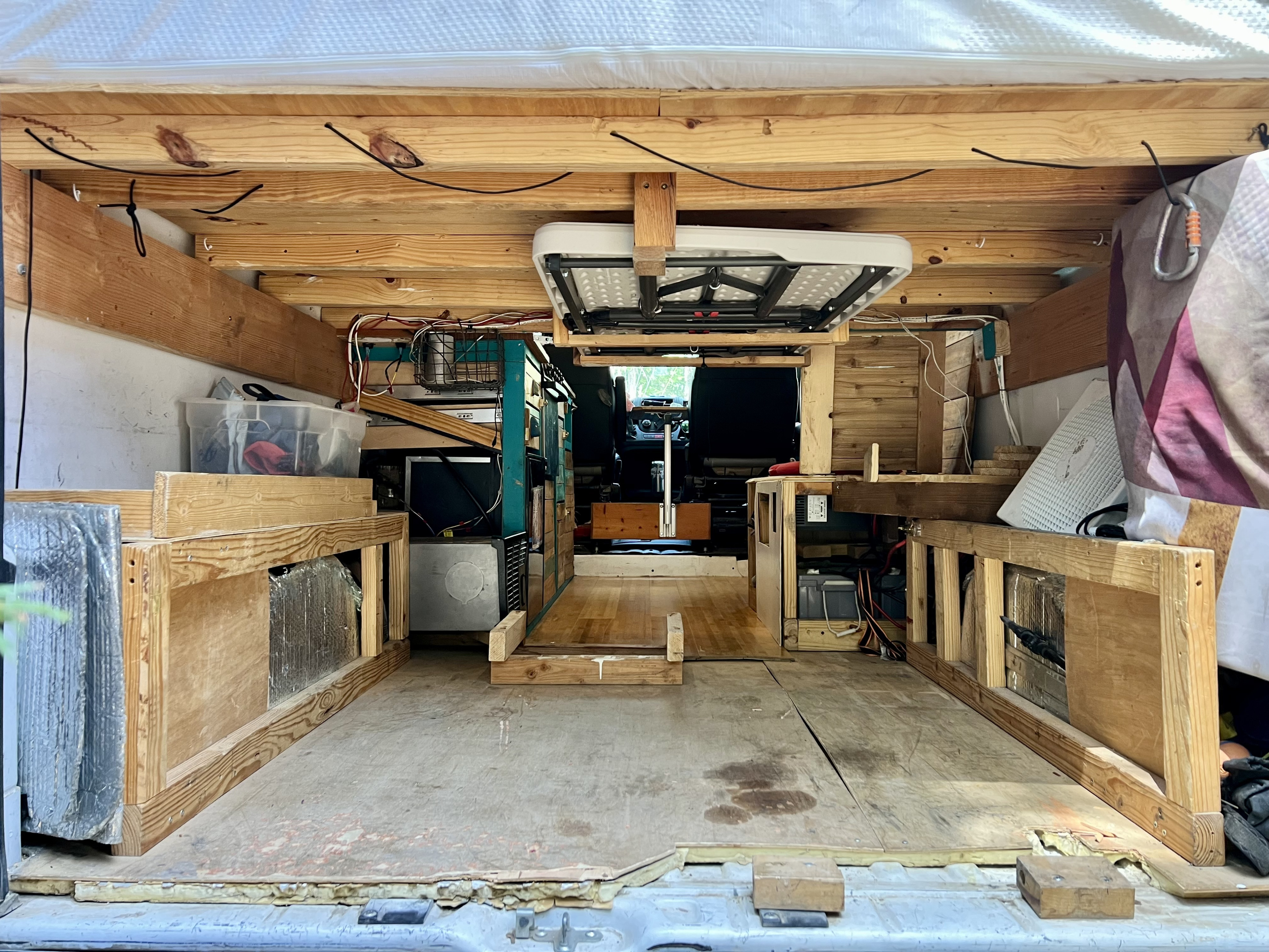 Rear interior of a DIY van conversion, ideal for an RV rental. Features rustic wood framing, storage, and an overhead table.. Dodge Promaster 2500 159 WB 2017