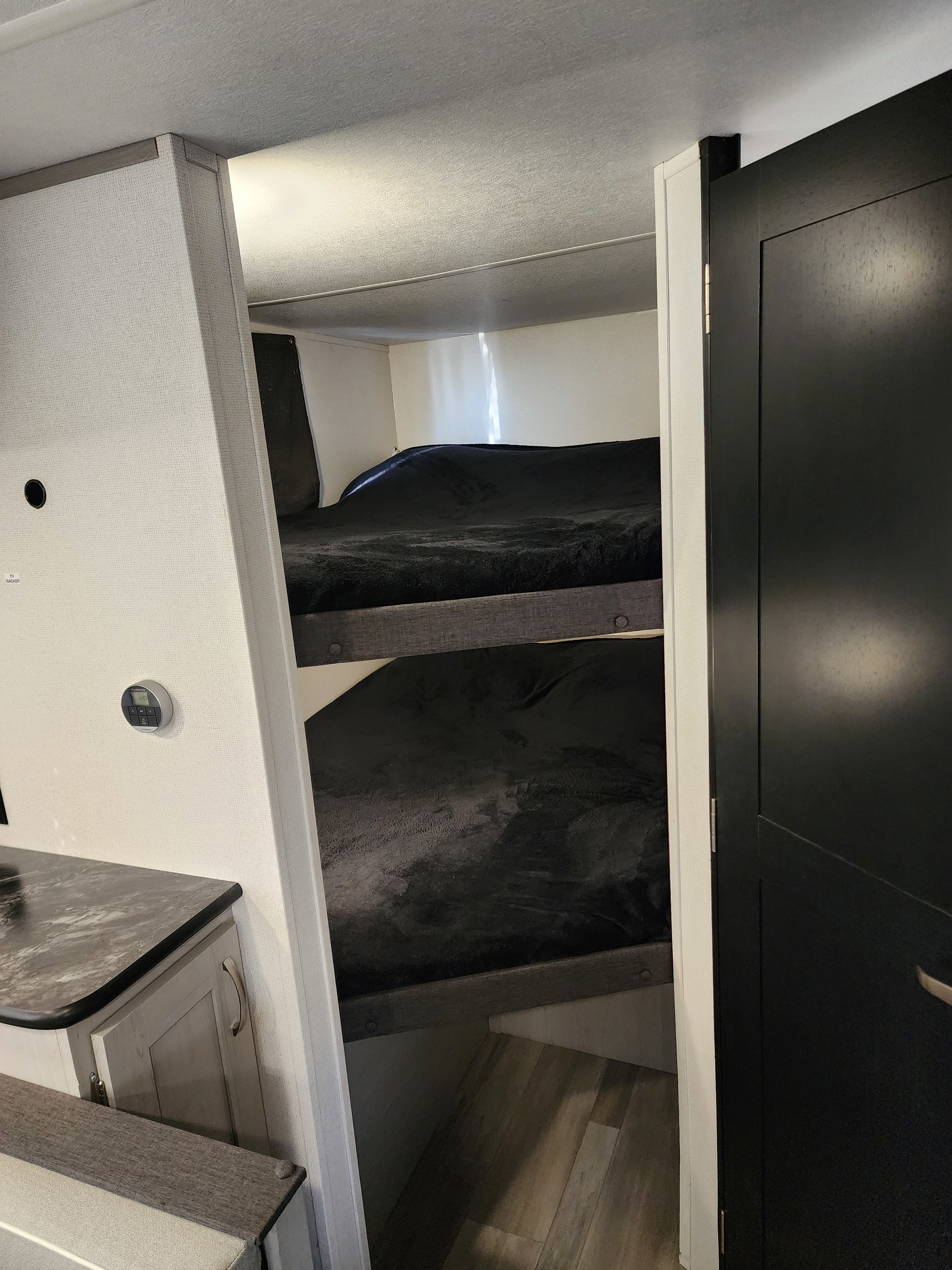 Cozy rv rental bunk beds with black bedding visible, plus a thermostat and counter, offering compact sleeping space.. Primetime Tracer 2022
