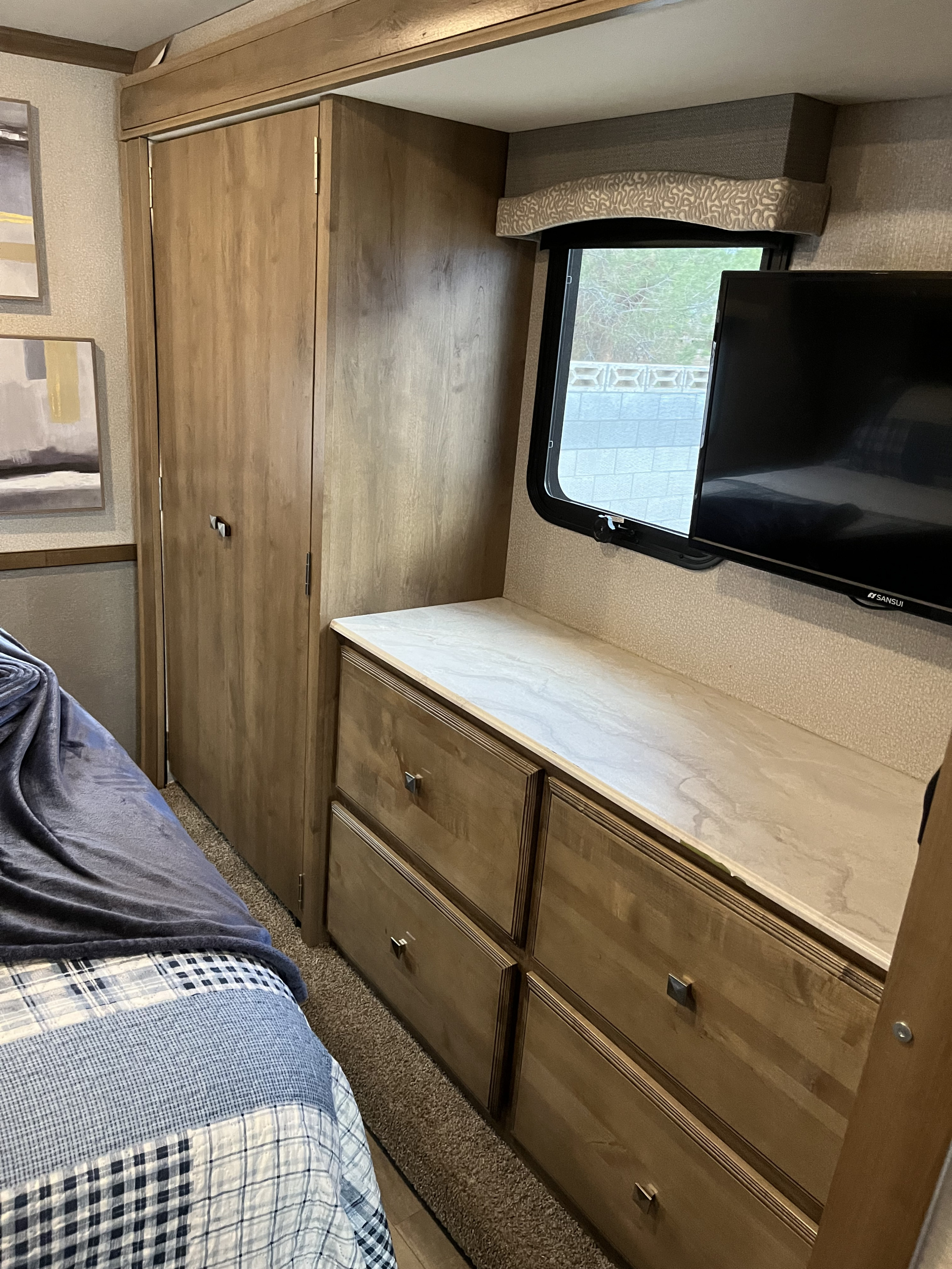This RV rental's bedroom offers ample storage with a wardrobe, dresser, TV, window, and cozy bed.. Fleetwood Flair 29M 2019