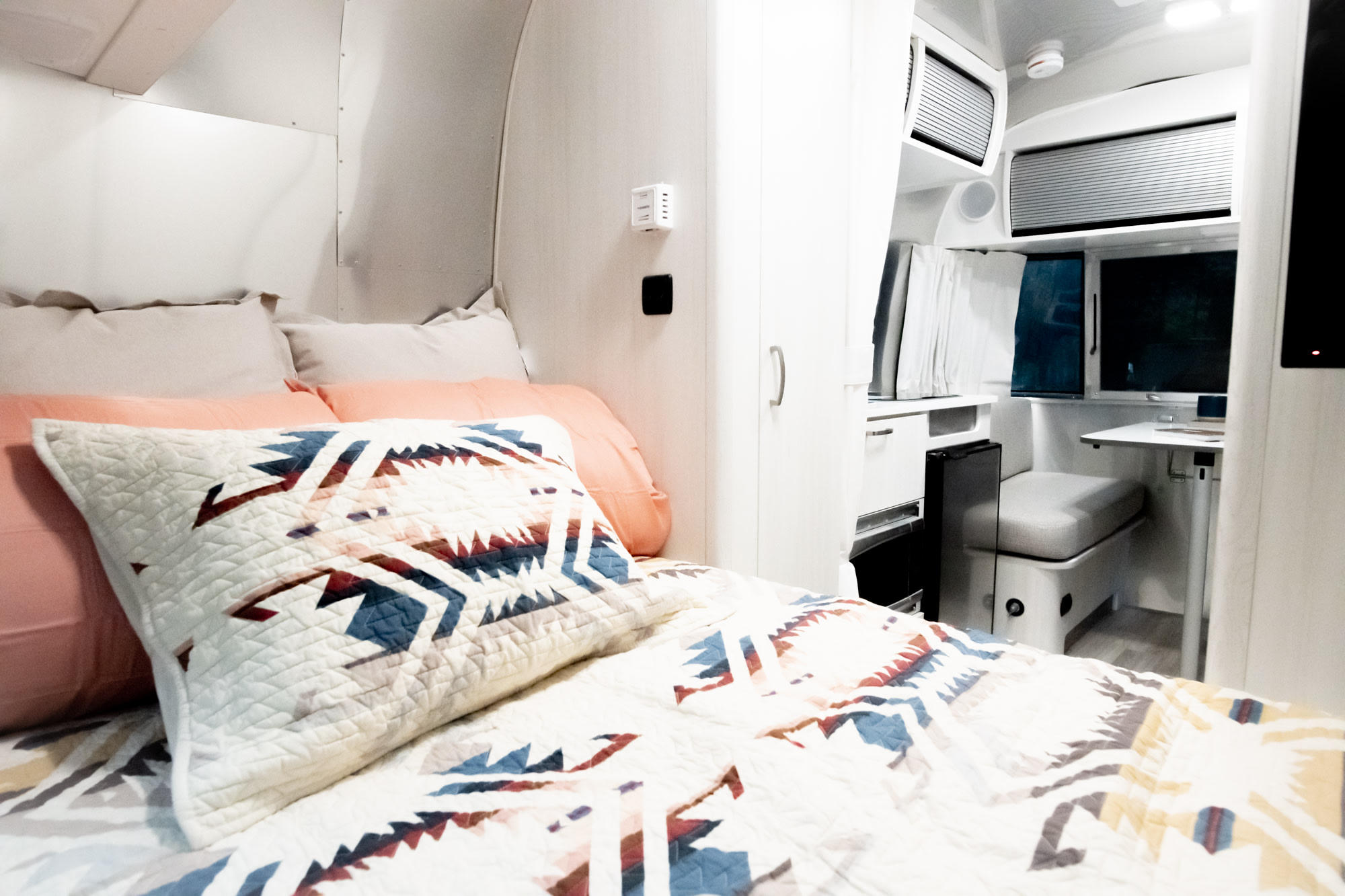 Modern RV rental interior showcasing a cozy bedroom with patterned bedding and a compact dining area.. Airstream Bambi 2022
