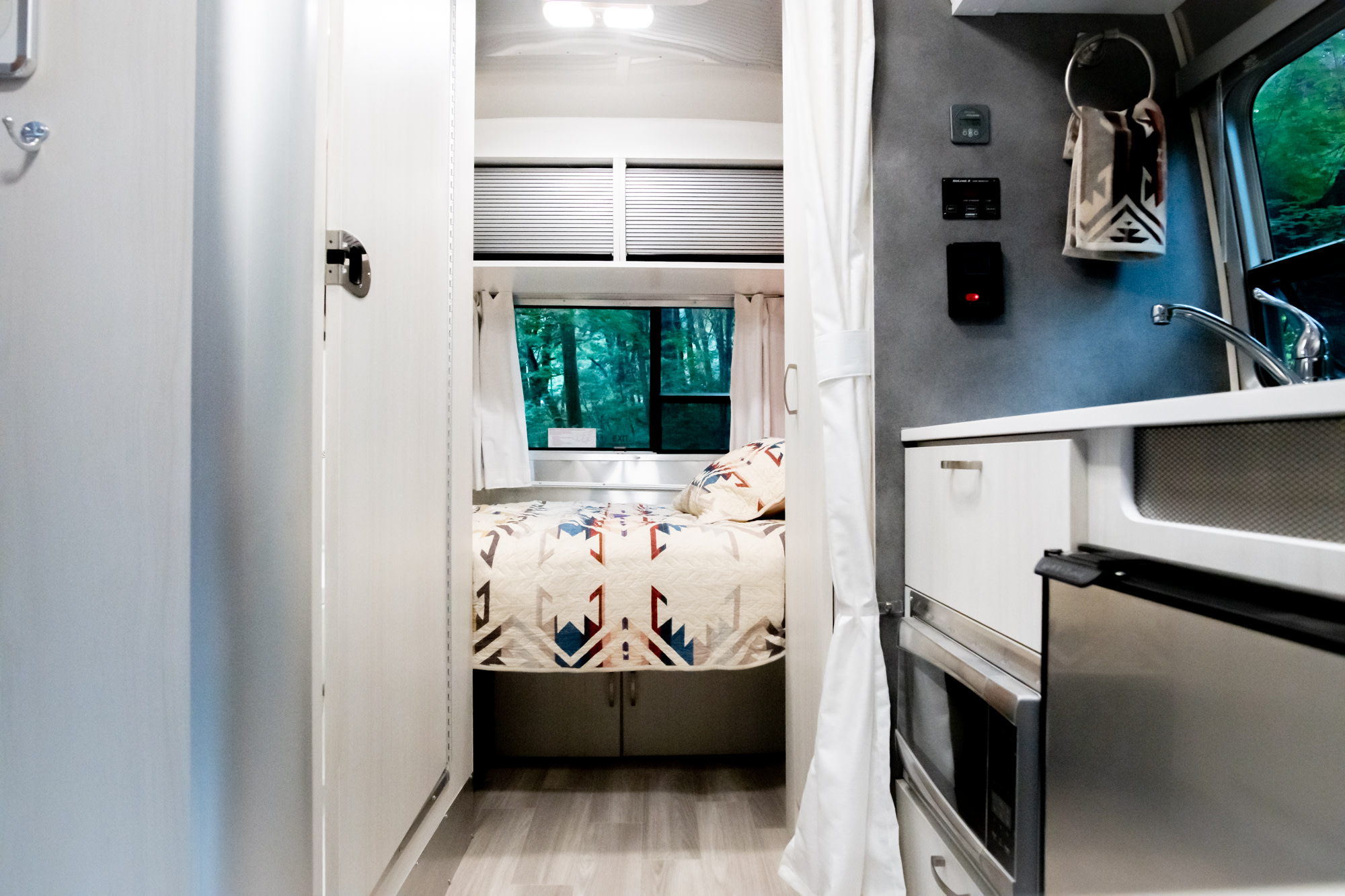 Bright & modern RV rental interior with a cozy bedroom, compact kitchen, & nature views. Ideal for travel!. Airstream Bambi 2022