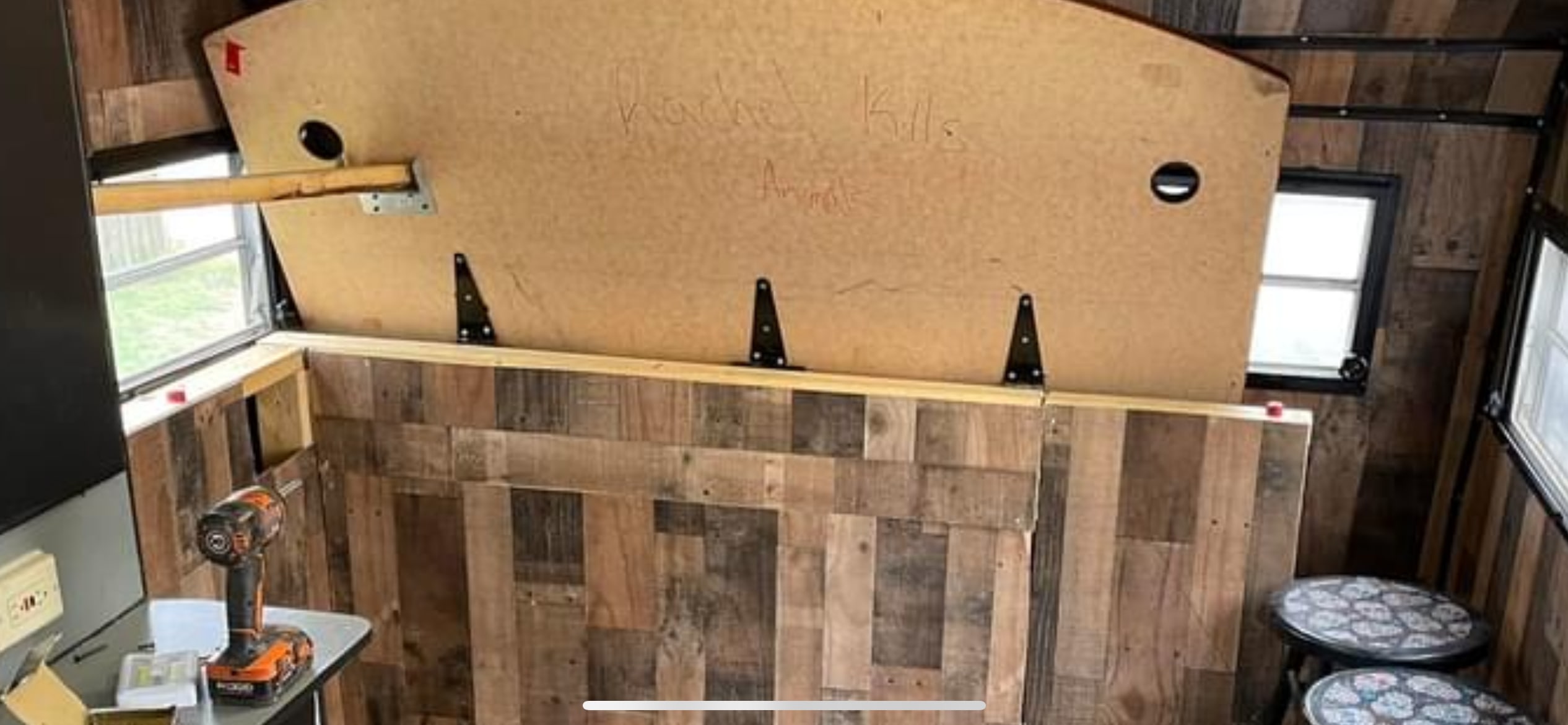 RV rental interior under DIY renovation, featuring reclaimed wood paneling, a propped-up convertible bed/table, and tools.. Sunline T2251 1985