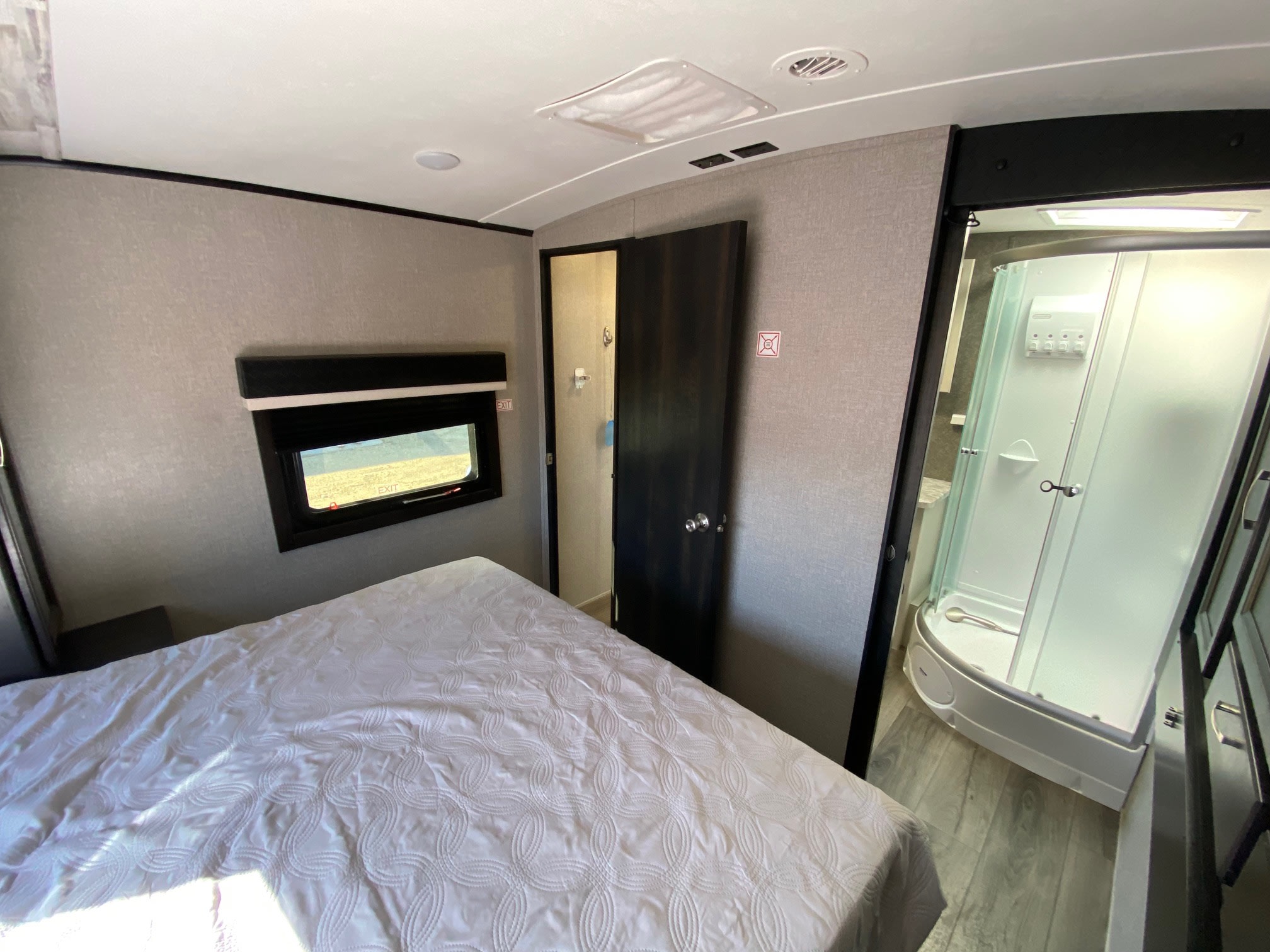 This RV rental's bedroom has a bed with a white comforter, a window, and a separate, curved shower unit.. Jayco White Hawk 2020