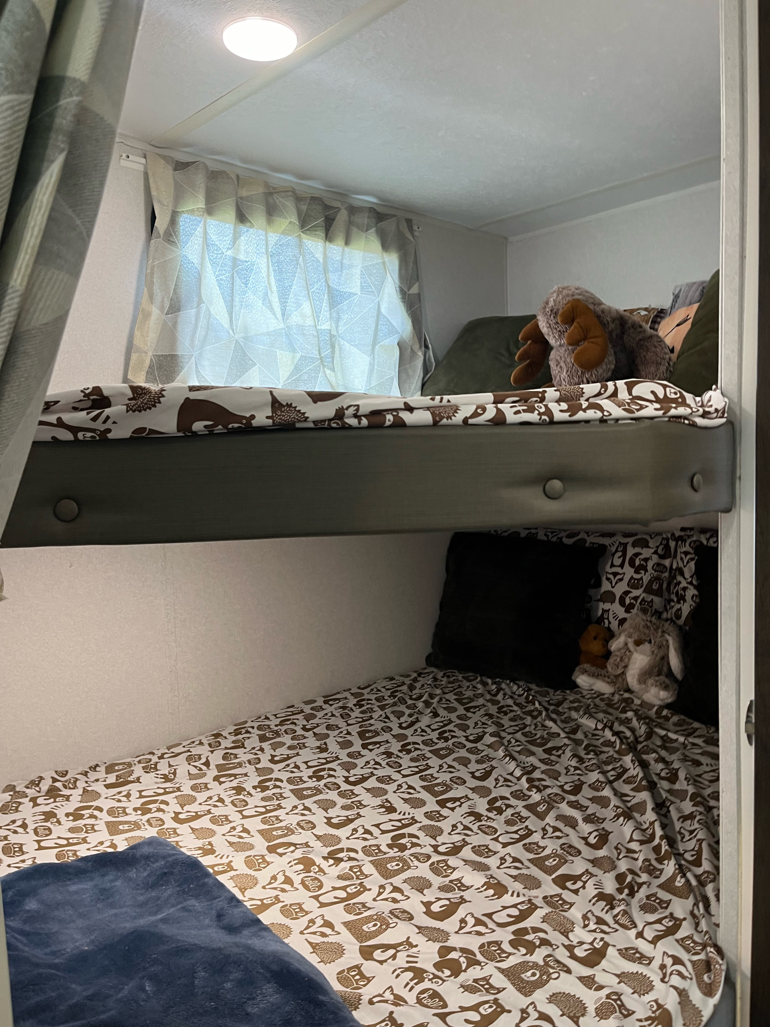 Cozy RV rental interior: bunk beds with whimsical woodland animal bedding, featuring plush toys. Bright ceiling light & window curtains.. Forest River Salem Cruise Lite 2019