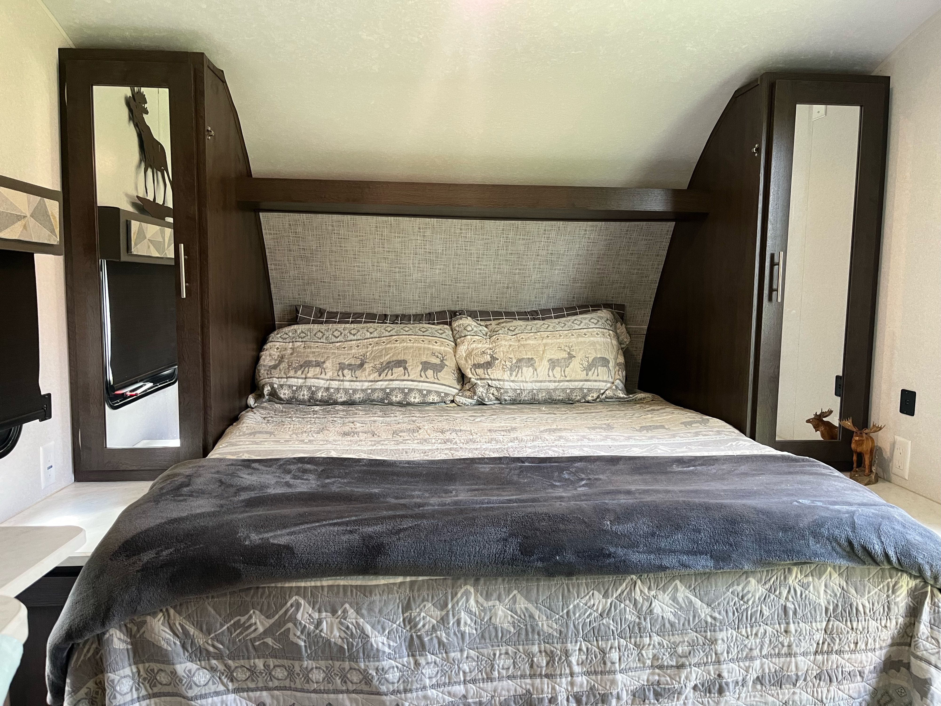 Inside an RV rental: a cozy bedroom with deer and mountain-themed bedding, dark wood cabinets, and charming moose decor.. Forest River Salem Cruise Lite 2019