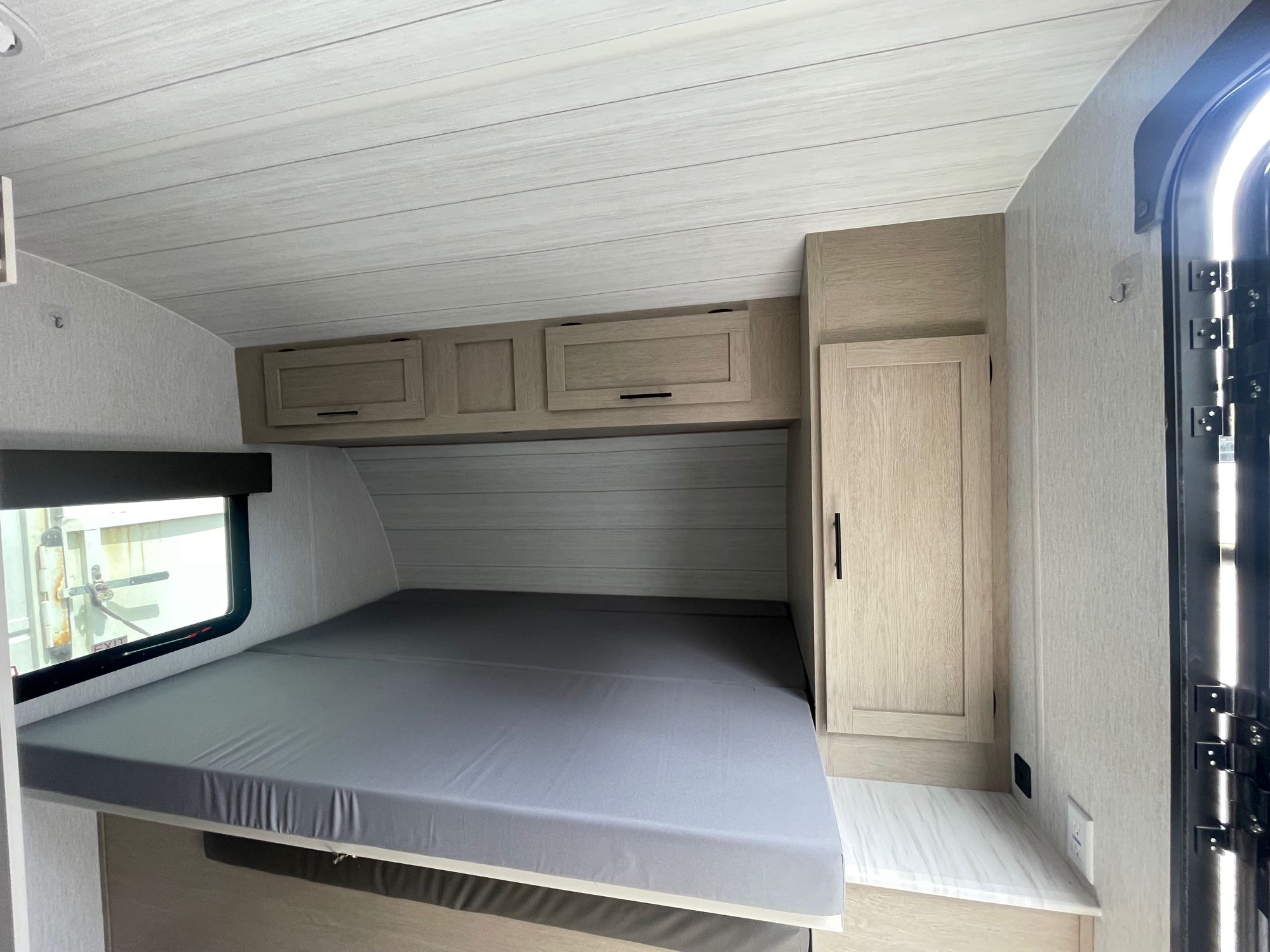 RV rental interior view: compact sleeping area with gray mattress, light wood storage cabinets, and entry door.. Forest River Salem Cruise Lite 2023
