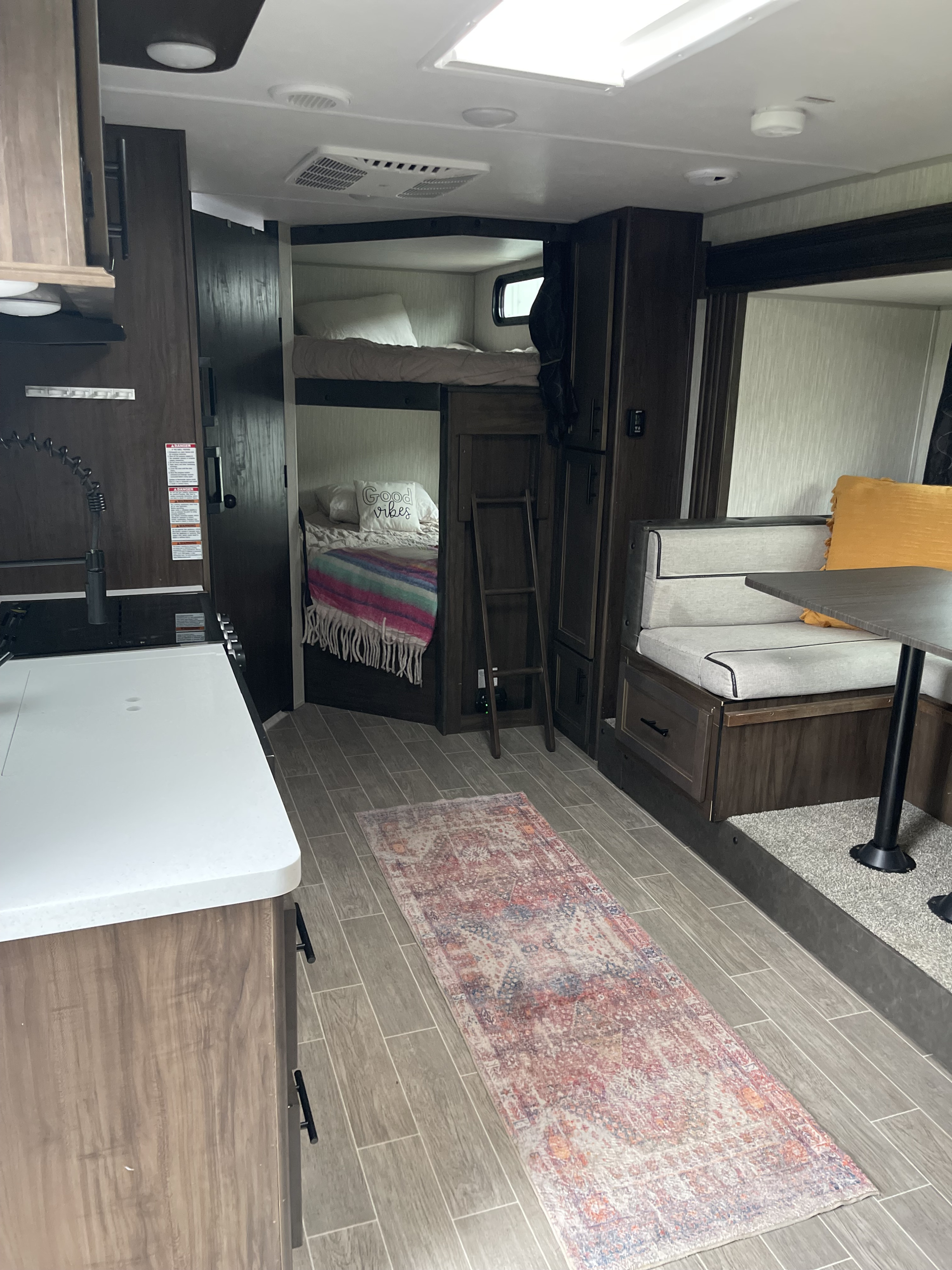 Bright RV rental interior: kitchen on left, bunk beds center, dining booth right. Perfect for travel adventures.. Forest River Cherokee Grey Wolf Black Label 2021