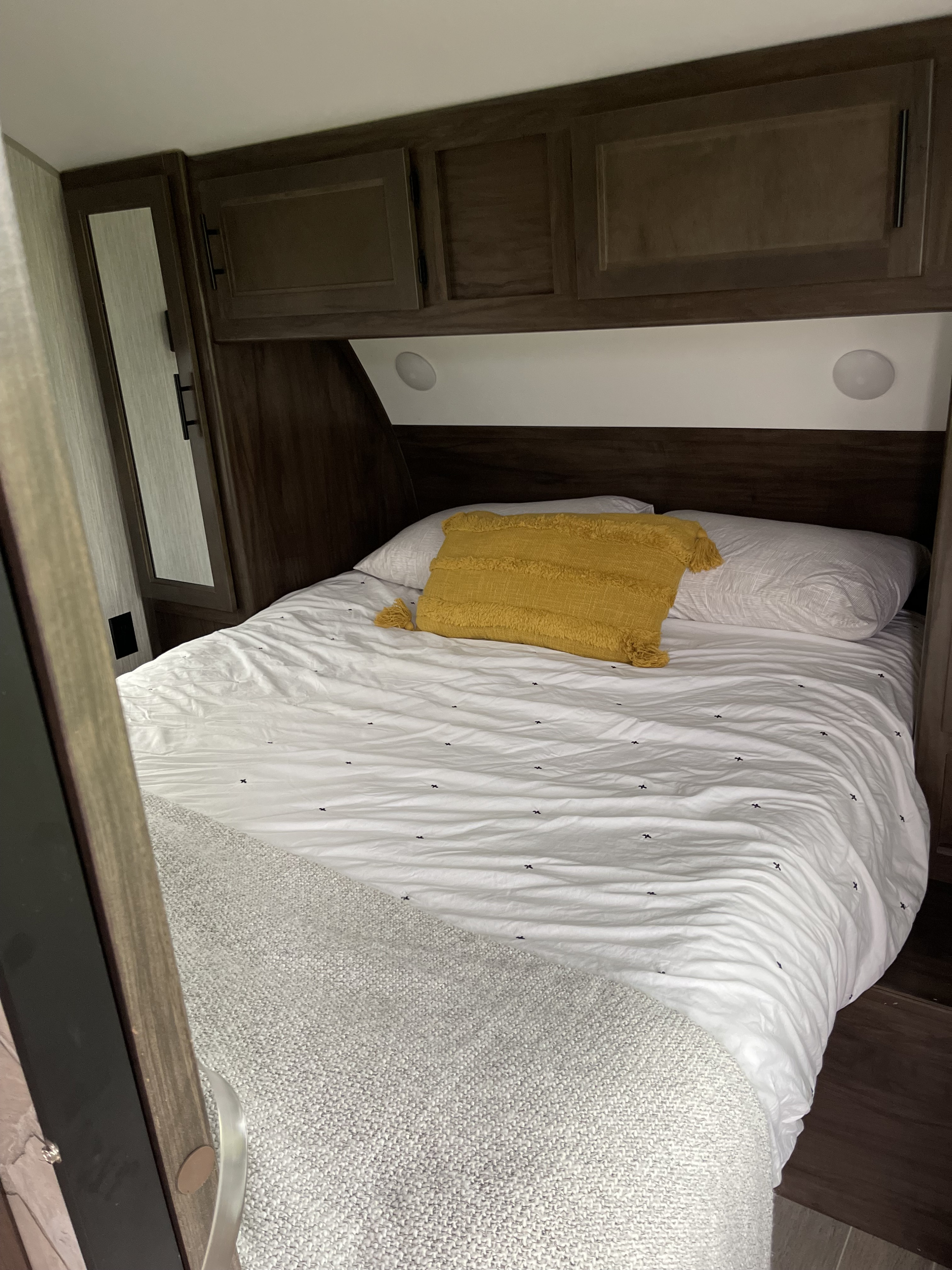 Cozy RV rental bedroom featuring a bed with white linen, a yellow pillow, and wood storage cabinets.. Forest River Cherokee Grey Wolf Black Label 2021