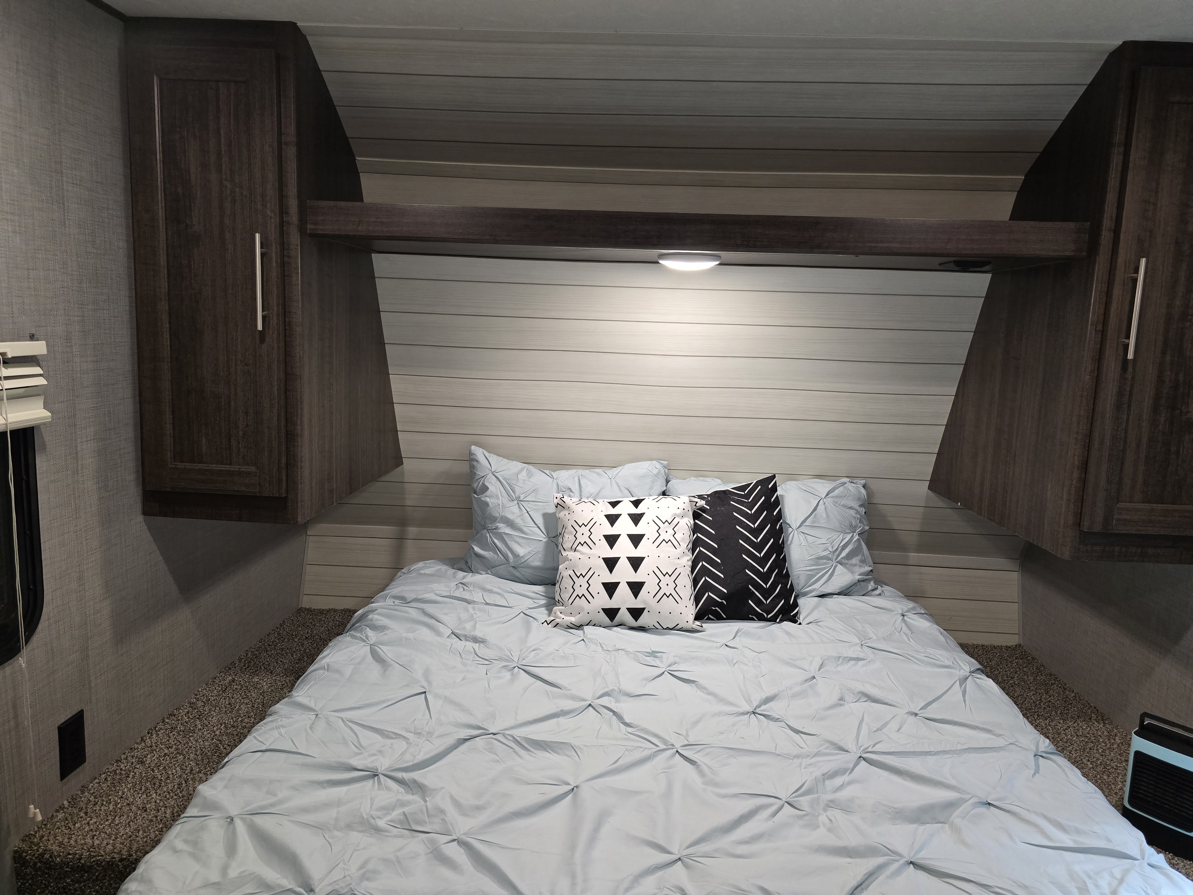 Cozy RV rental bedroom featuring light blue bedding, overhead cabinets, soft lighting, and patterned throw pillows.. Crossroads RV Zinger 2018