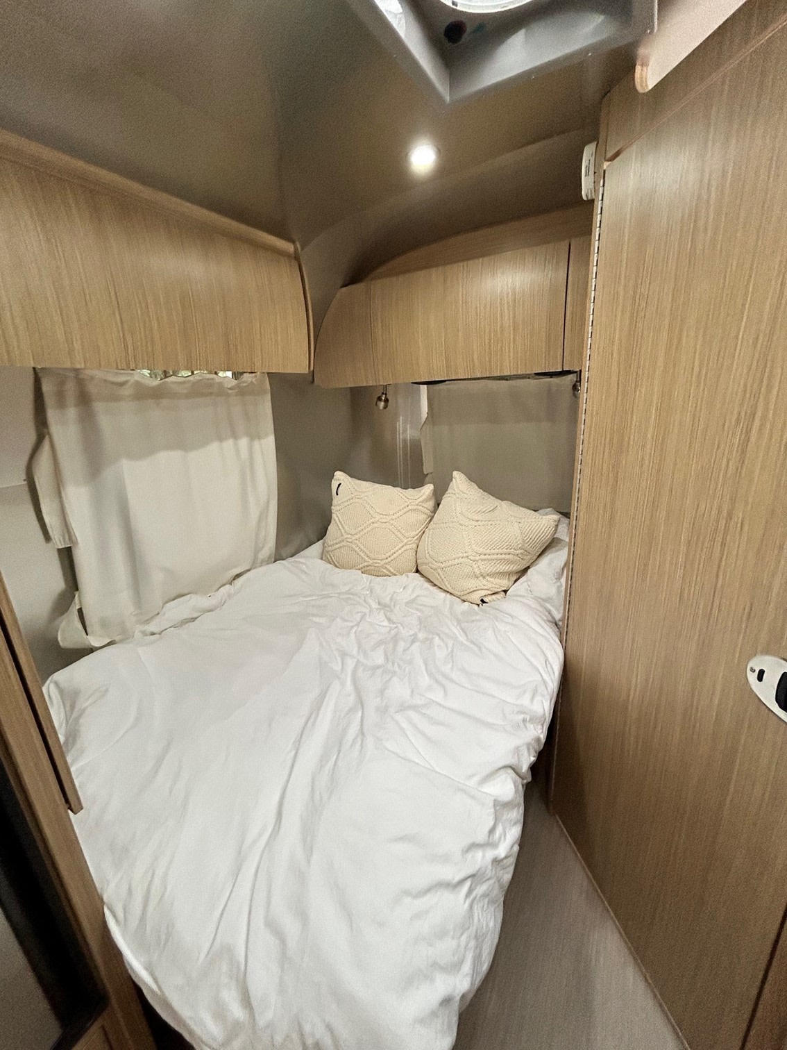 Cozy RV rental bedroom with white bedding, knitted pillows, and light wooden cabinets, perfect for compact travel.. Airstream Flying Cloud 2017